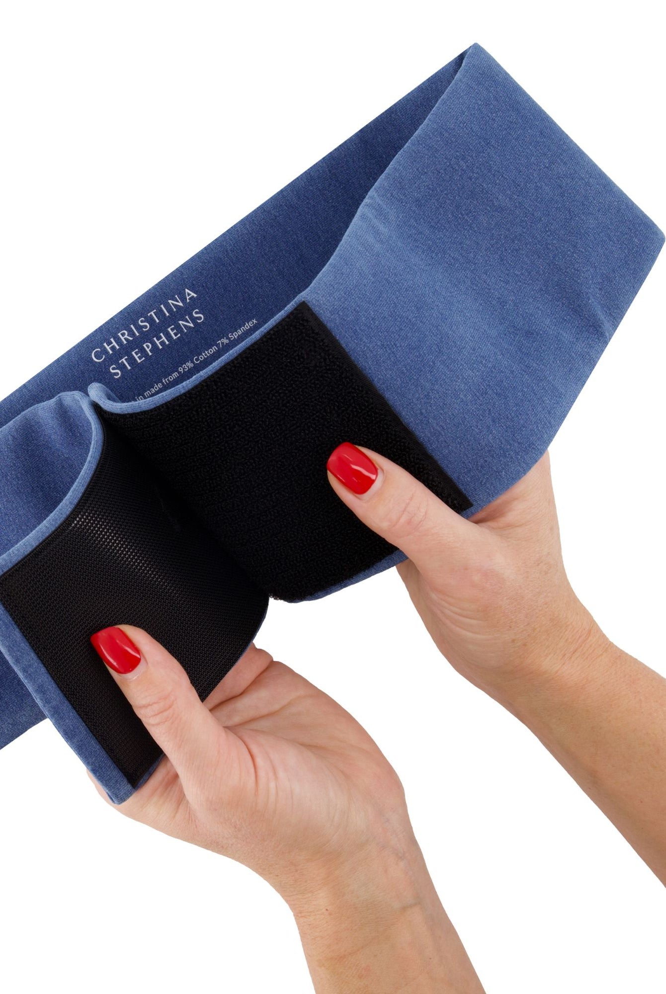 Wheelchair Leg Strap shown in denim blue and black fabric, being held to display its soft material and adjustable design. The product features a secure velcro closure and comfortable padding for wheelchair users to maintain proper leg positioning.