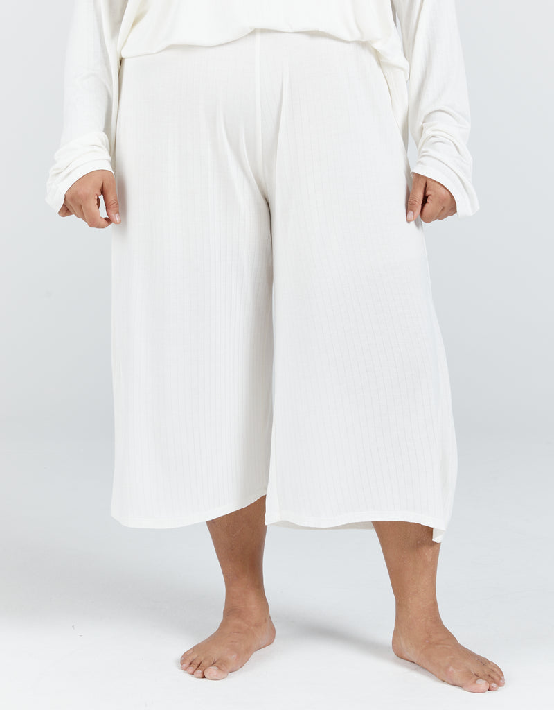 Standing female with brunette hair up in a bun is wearing an ivory bamboo leaf back top with long sleeves. She is also wearing a cropped wide leg pant made from the same fabric. Christina Stephens Adaptive Clothing Australia