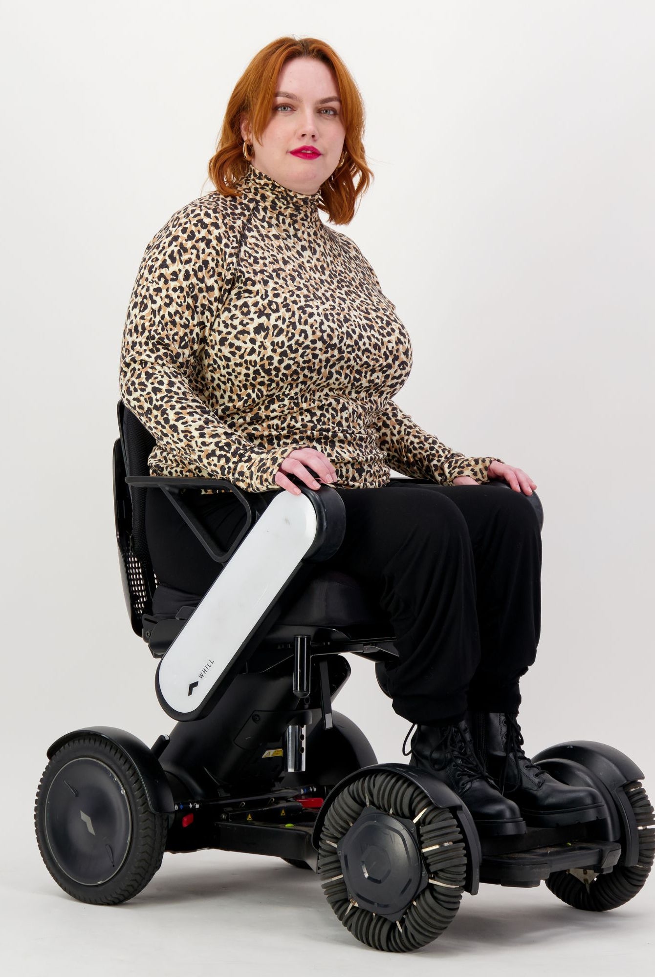 Maggie Thermal Top shown on a model seated in a modern white mobility device, featuring a stylish leopard print pattern with turtleneck design. The thermal top demonstrates adaptive wear comfort against a clean white background.