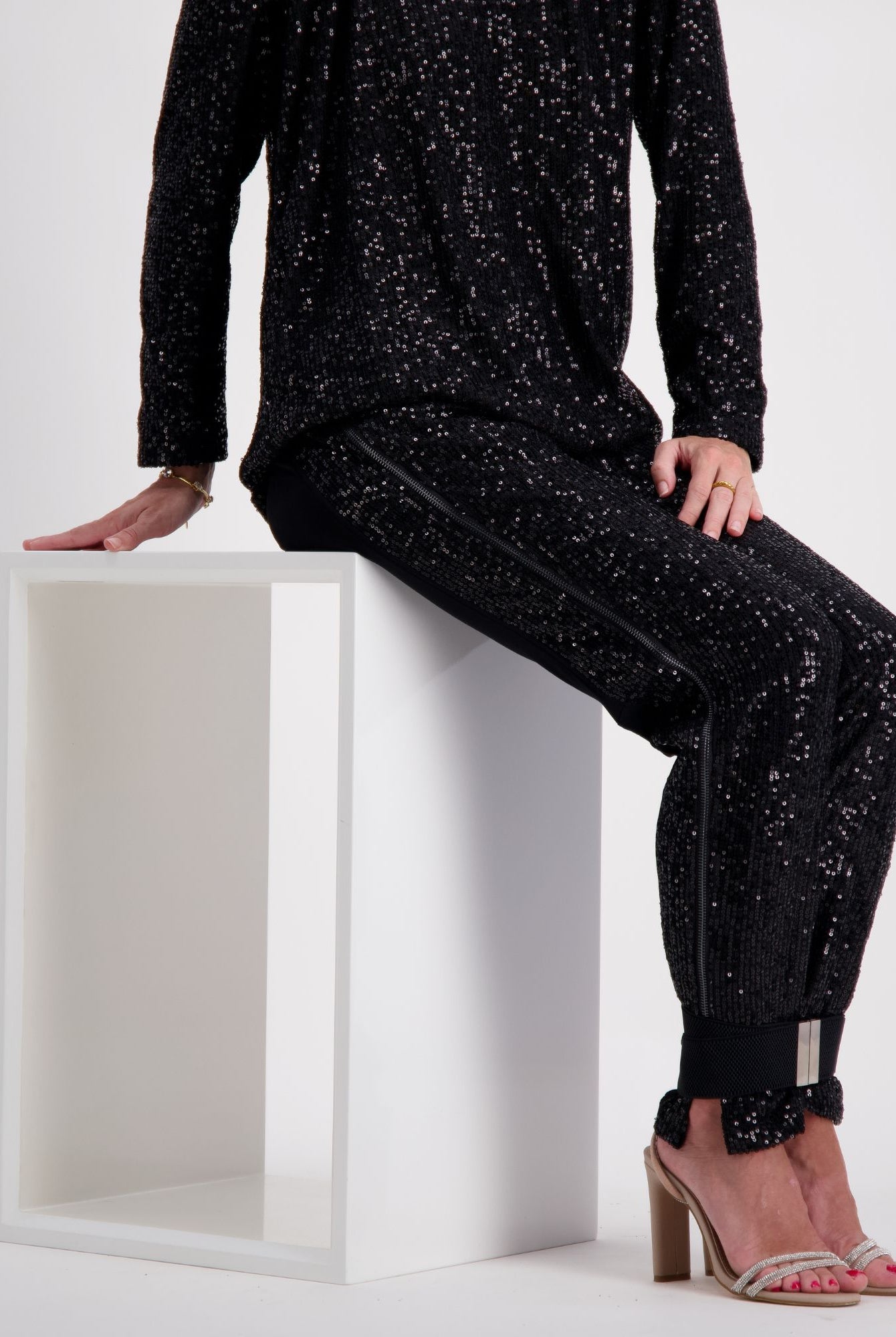 Suzie Q Seated Pants Sequins shown on a white pedestal, featuring sleek black sequined fabric with a comfortable adaptive design. The pants showcase elegant sparkle detail from hip to ankle, with a relaxed fit and specialized accommodations for medical devices.