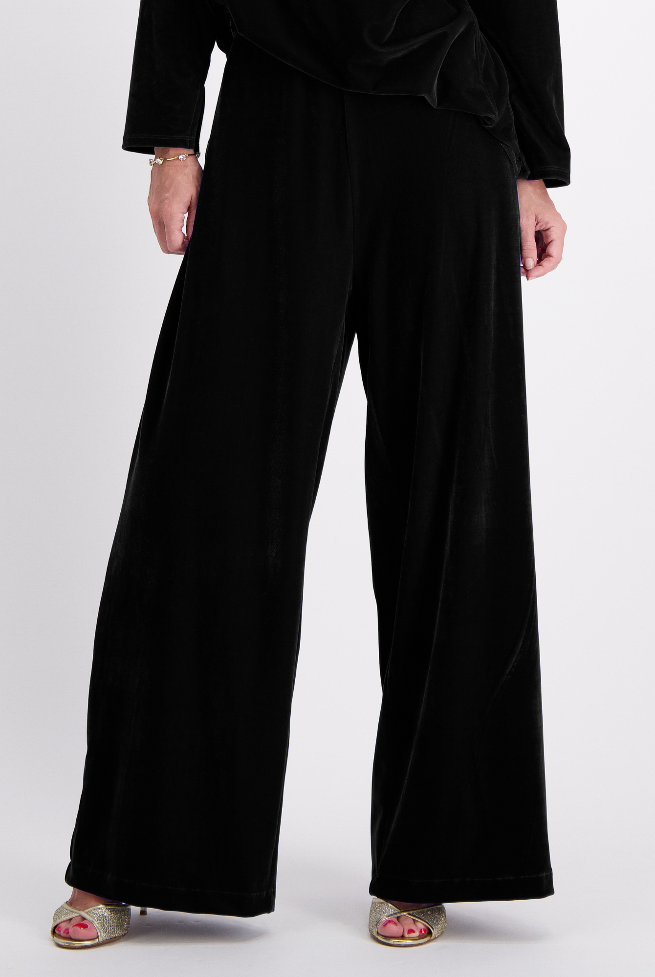 Jessie Wide Leg Velvet Pants in luxurious black velvet, featuring a flowing wide-leg silhouette, side pull tabs, and floor-length design. Elegant evening wear pants shown with metallic sandals against a light gray background.