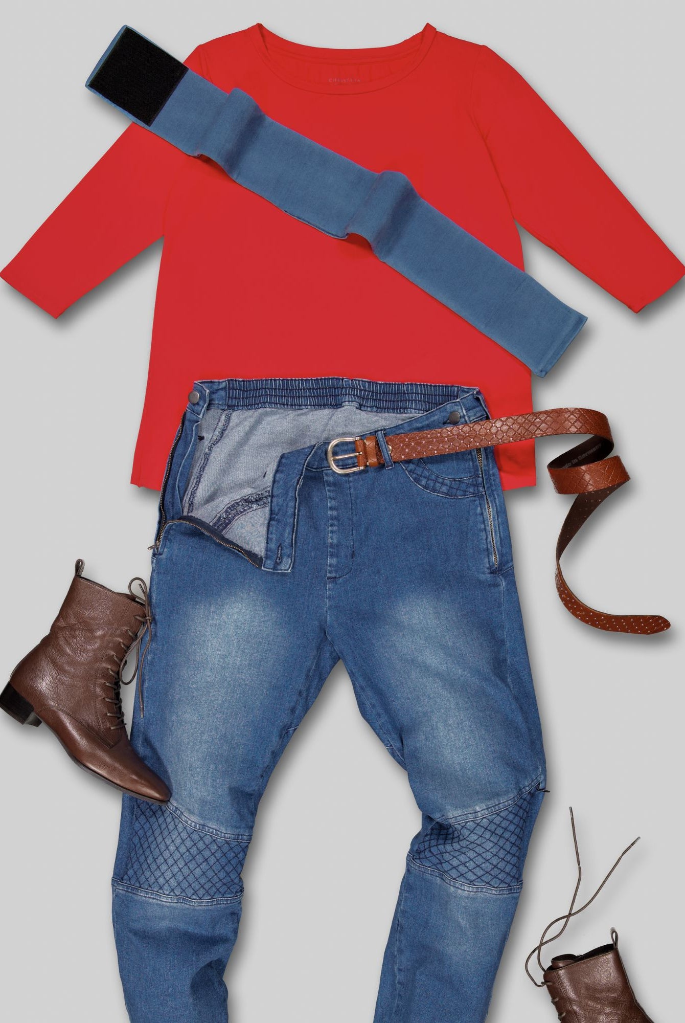 Wheelchair Leg Strap shown with red sweater, adaptive denim jeans, brown leather belt and boots in a flatlay composition. The denim blue strap features a secure black fastening mechanism for comfortable wheelchair positioning.