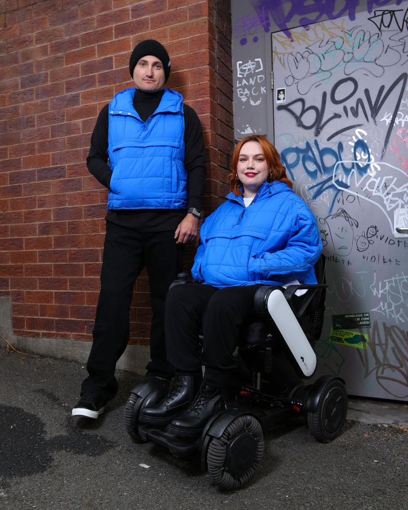 Standing male and seated female wearing cobolt blue puffer vest and jacket. Christina Stephens Adaptive Clothing Australia. 