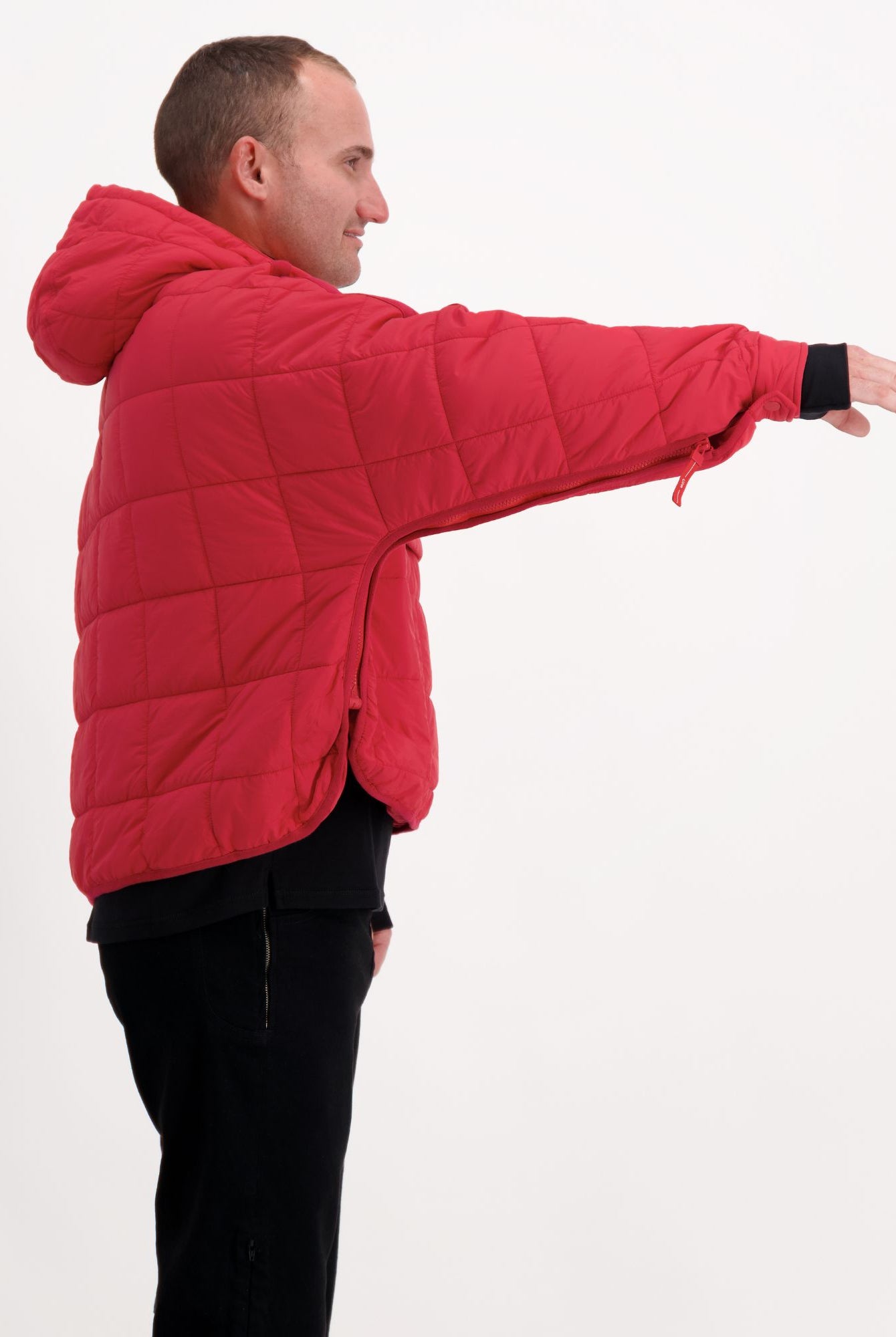Elly Universal Puffer Jacket shown from side view in bright red, demonstrating adaptive design with quilted pattern. Model wearing black pants displays jacket's comfortable fit and extended arm mobility against white background, highlighting practical features for wheelchair users.