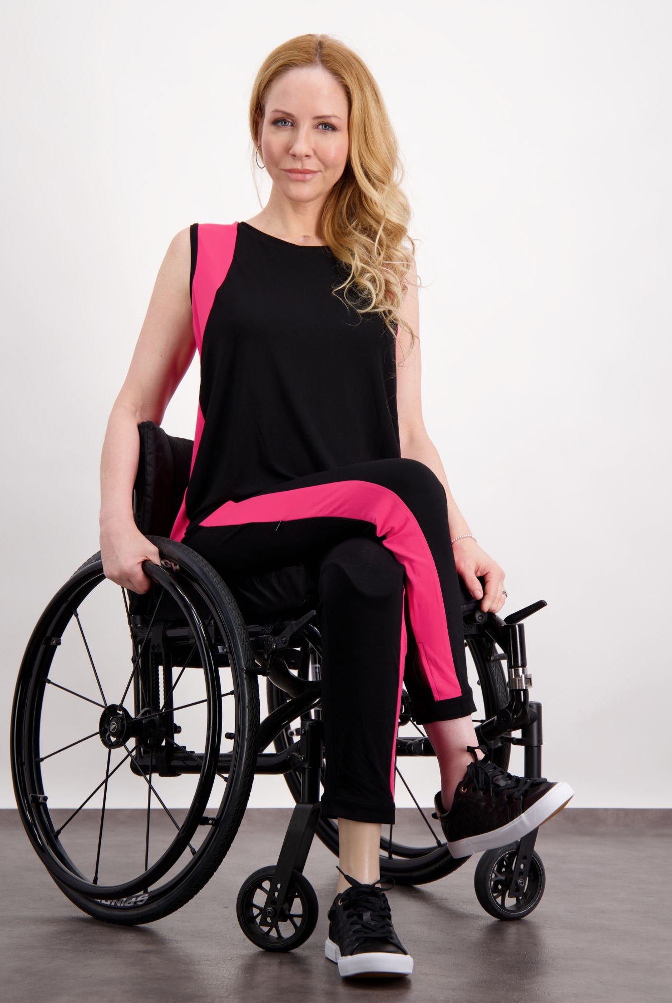 Lauren Sleeveless Physio Top shown in black with vibrant pink accents, displayed on a seated model against a white background. The sleeveless design features modern color blocking and a relaxed fit, perfect for athletic and casual wear.