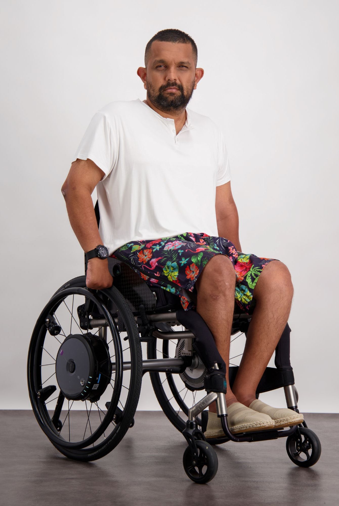 Nick A-Line T-Shirt shown on a wheelchair user against a light background. The white adaptive bamboo t-shirt is paired with colorful patterned shorts. The casual look demonstrates the shirt's versatility and comfortable fit while maintaining a stylish appearance.