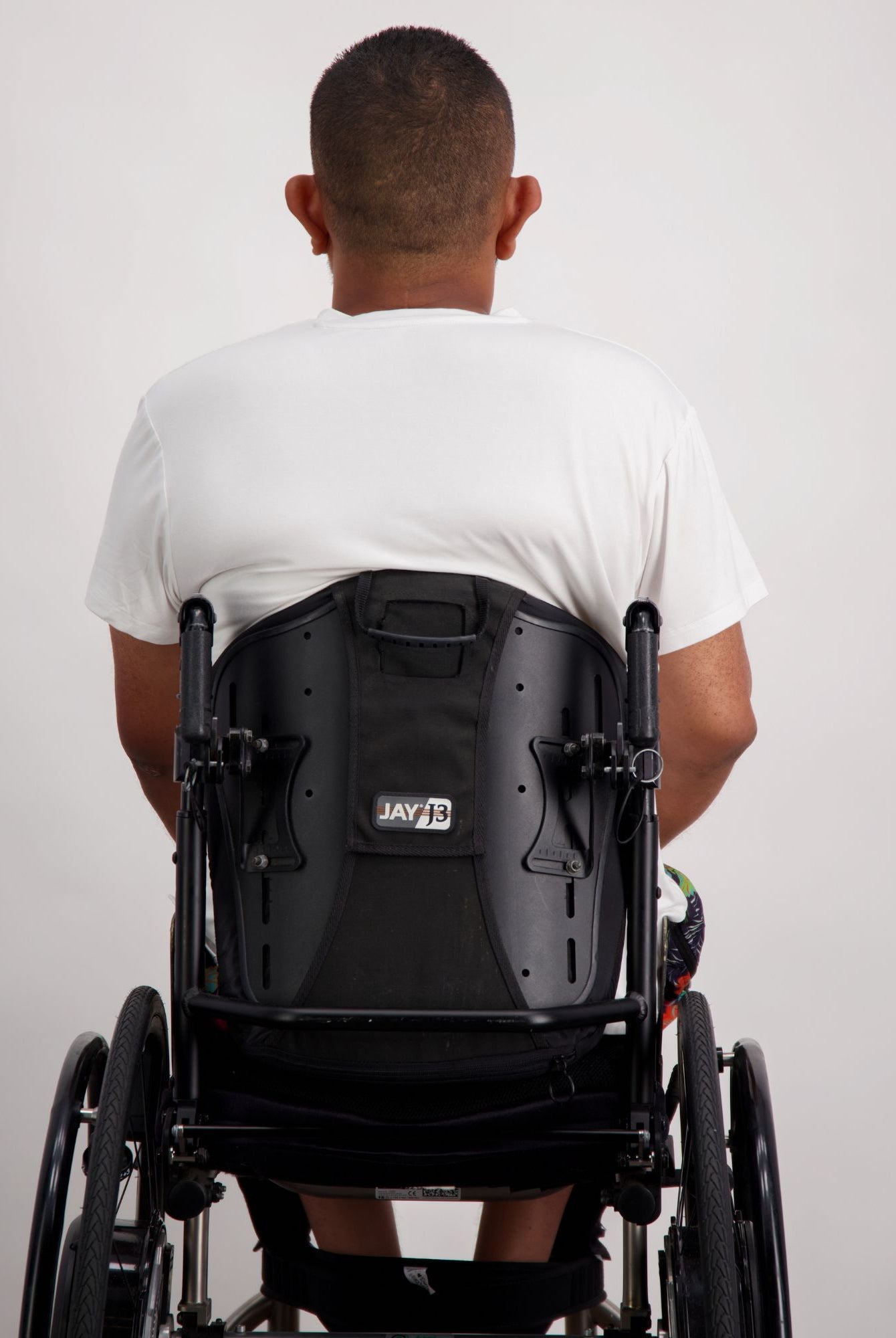 Back view of Nick A-Line T-Shirt in white bamboo fabric, shown on a person seated in a black wheelchair. The adaptive t-shirt demonstrates a comfortable, relaxed fit with clean lines and stretchy material suitable for everyday wear.