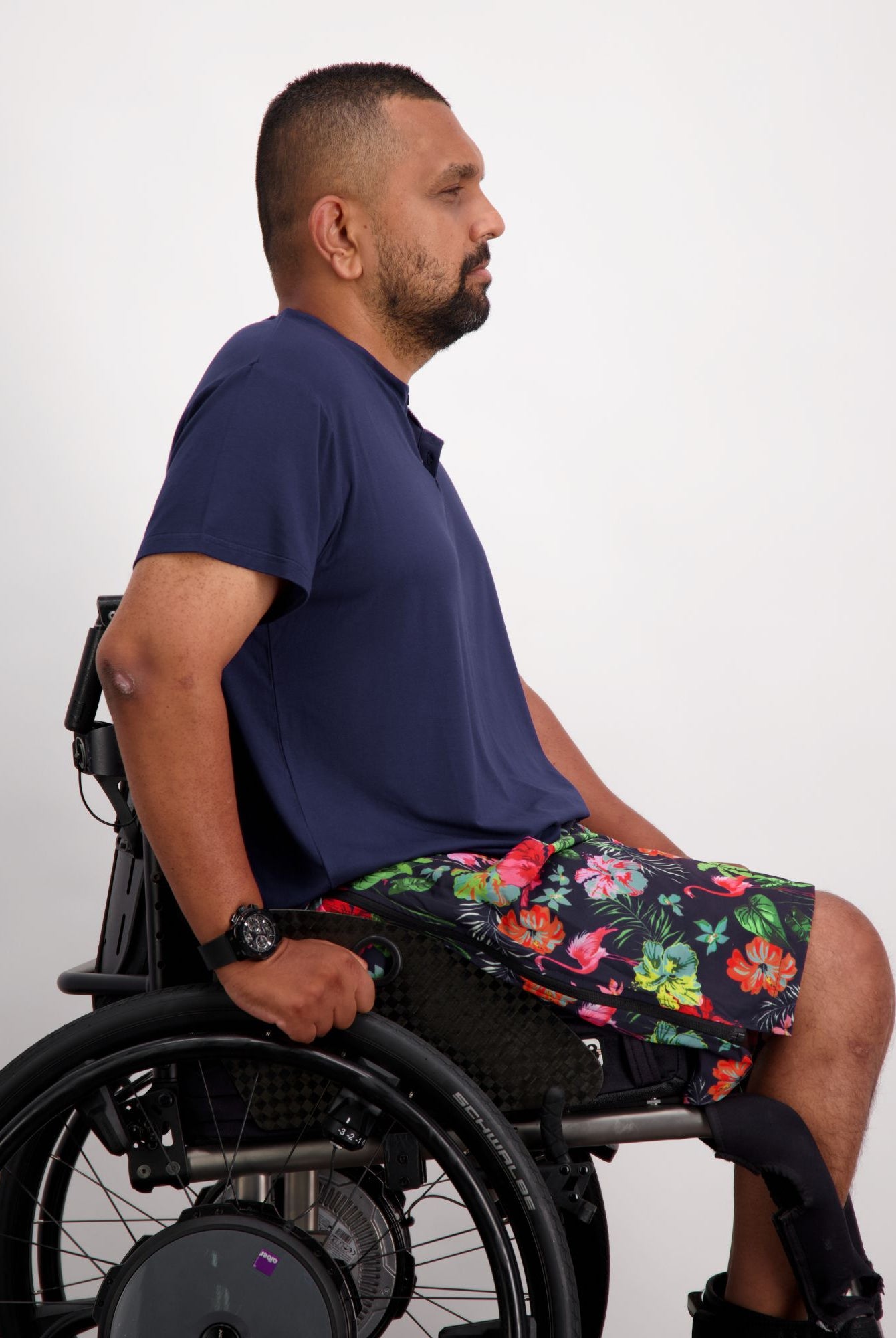 Navy Nick A-Line T-Shirt shown on a wheelchair user against white background, paired with floral print shorts. The adaptive bamboo shirt features a comfortable A-line cut, demonstrating its sensory-friendly design and versatile styling potential.