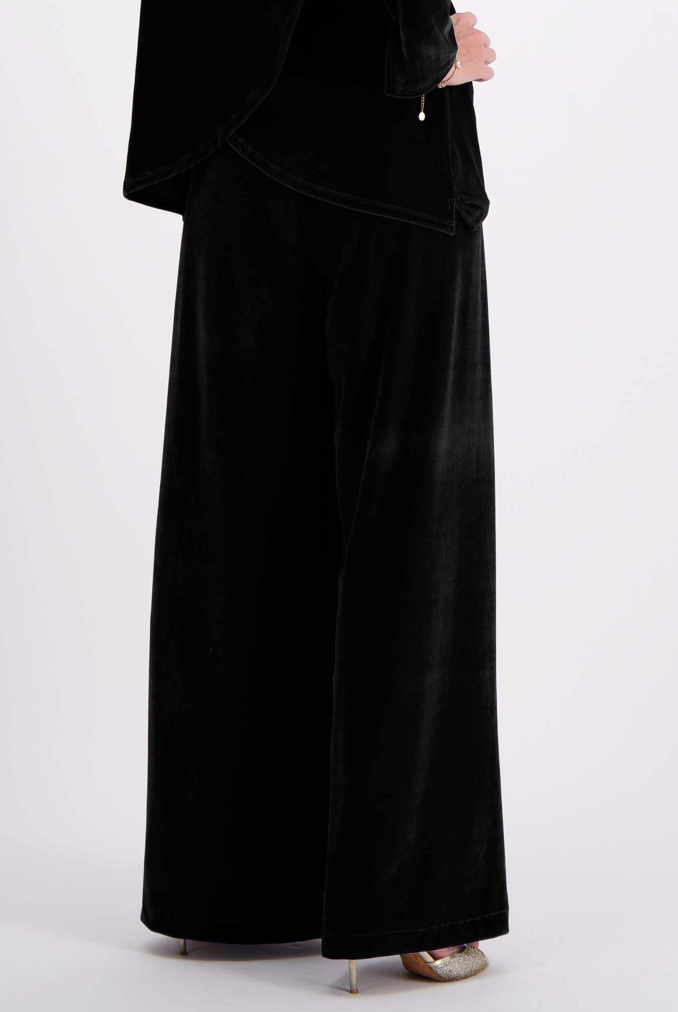 Jessie Wide Leg Velvet Pants shown in luxurious black velvet fabric, featuring an elegant wide-leg silhouette and side pull tabs, styled with metallic heels against a white background.