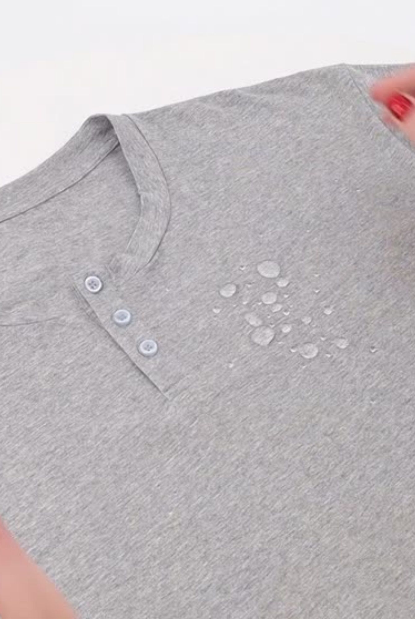 Nick A-Line Tee in heather gray featuring spill-resistant technology, with water droplets beading on the surface. Close-up view showing three-button henley neckline detail and the fabric's water-repellent properties in action.