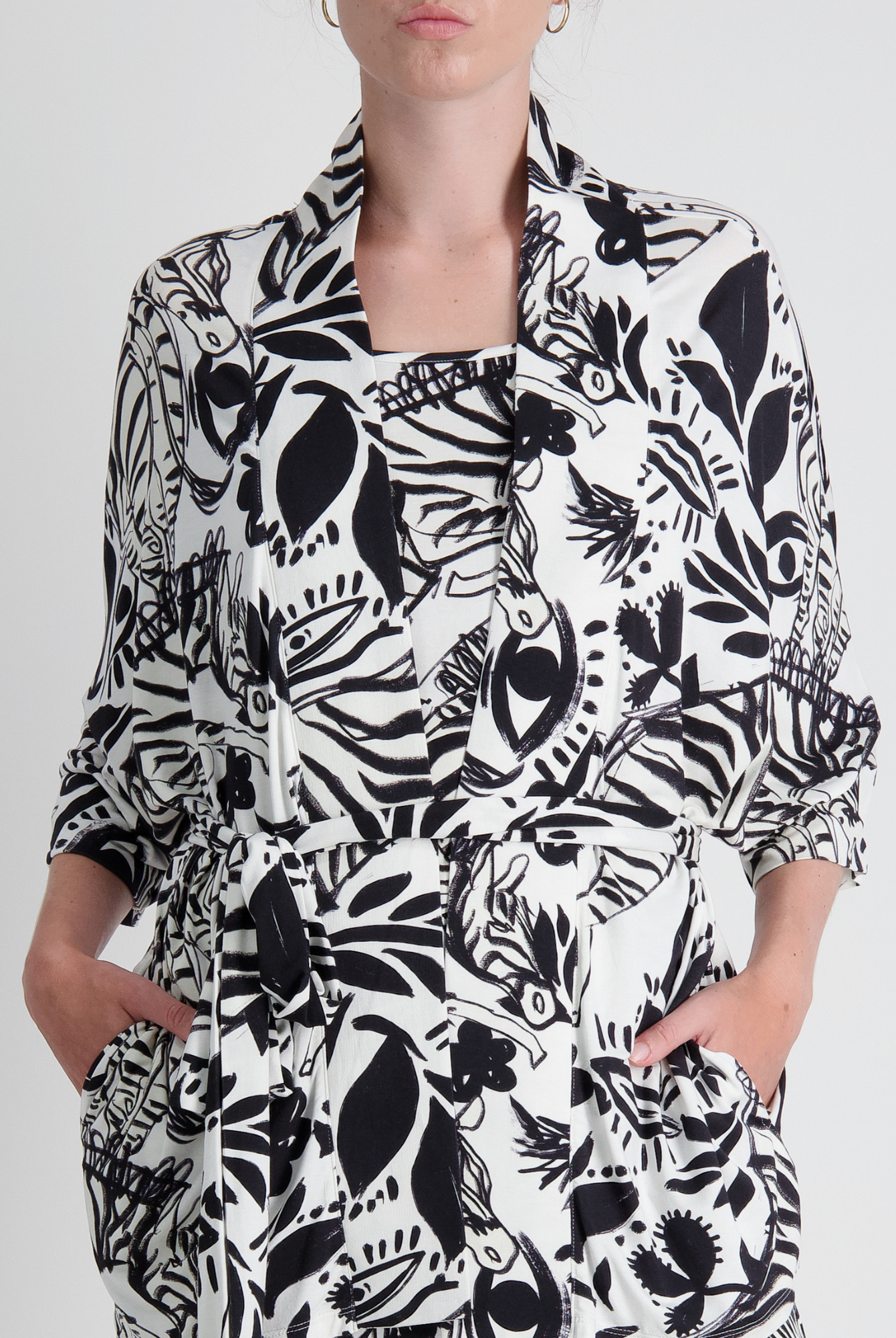 Georgie Adaptive Kimono featuring a bold black and white botanical print with abstract floral and leaf patterns. The cropped design showcases wide sleeves, front pockets, and a collared neckline, styled in a modern, seated-friendly silhouette against a light background.