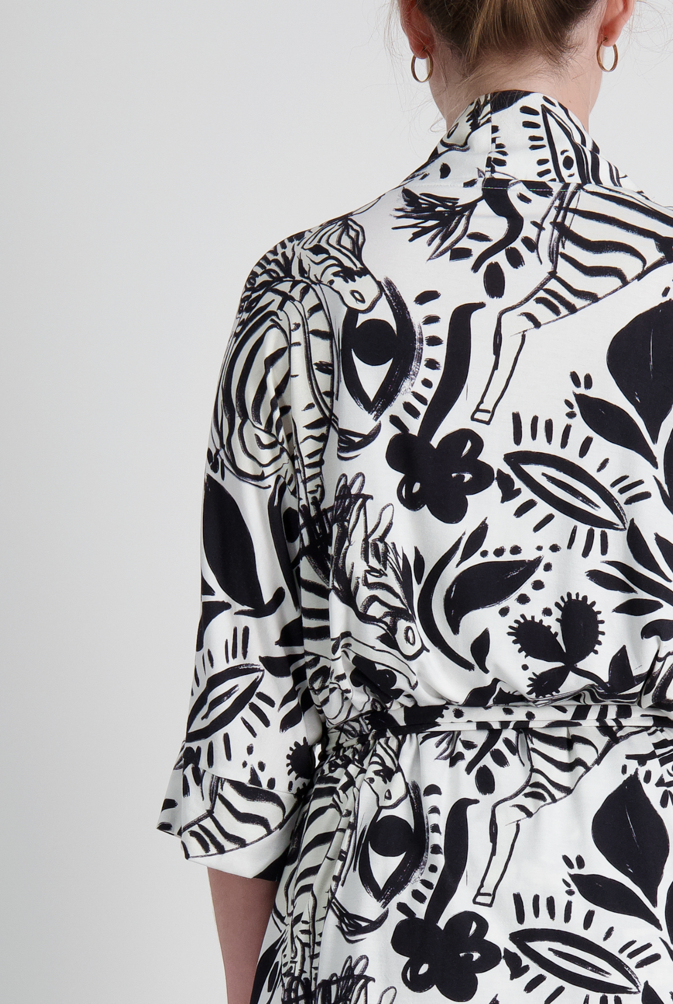 Back view of the Georgie Adaptive Kimono featuring a striking black and white botanical print pattern, showcasing wide sleeves and seamless design on a light background. The cropped style displays modern, bold floral and leaf motifs with artistic line work.