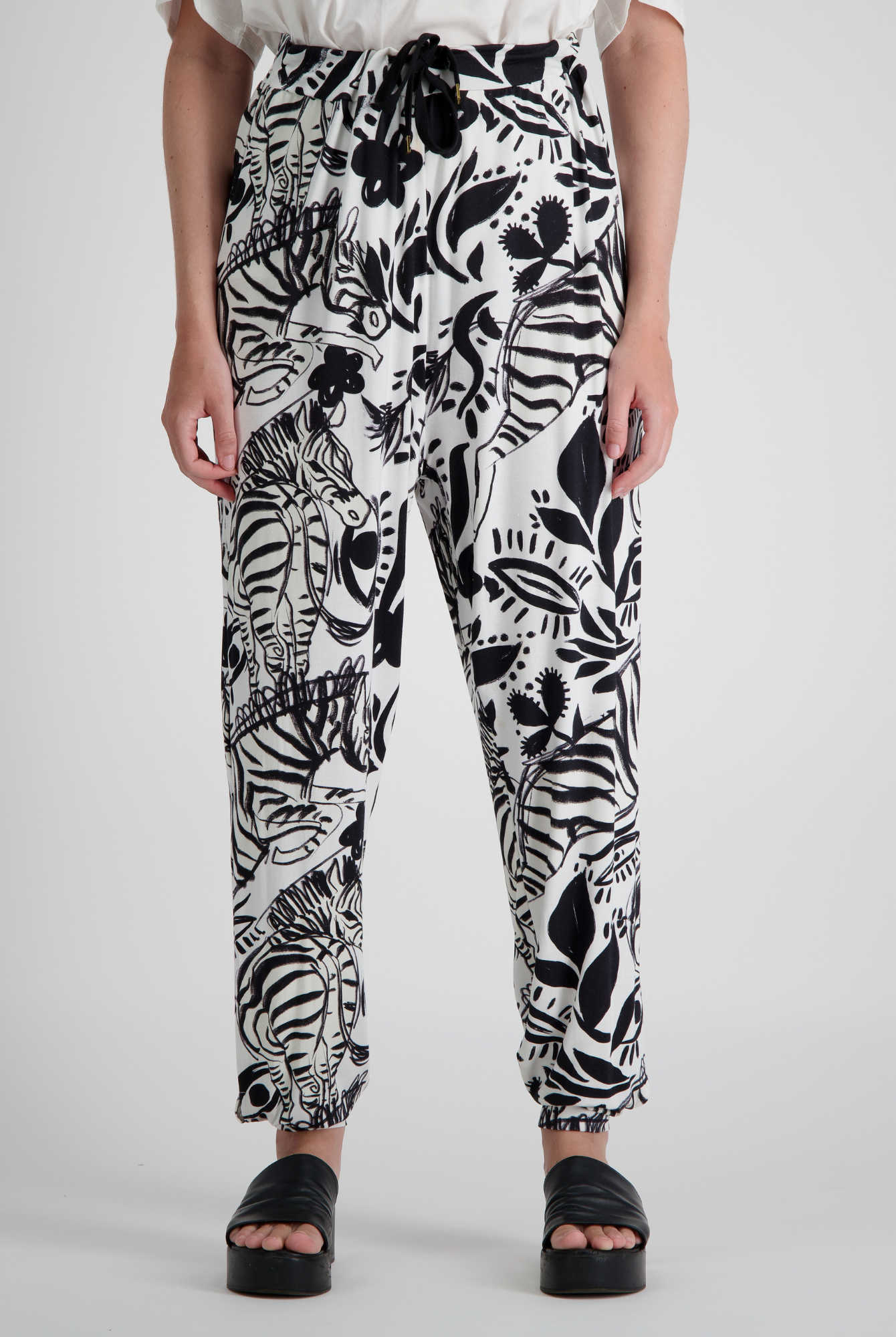 Roisin Adaptive Slouch Pants showcased in striking black and white botanical print on bamboo fabric, featuring tapered legs, drawstring waist, and relaxed fit. Styled with black platform sandals against light grey background.