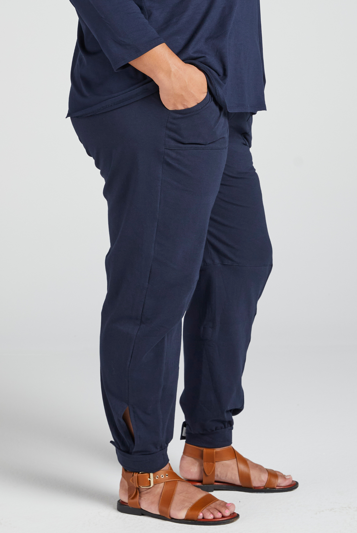 Navy blue Tapered Track Pants with Hidden Pouch shown from side view, featuring tapered leg design, side pocket detail, and paired with brown leather sandals. Comfortable fit demonstrates practical functionality and modern casual style.