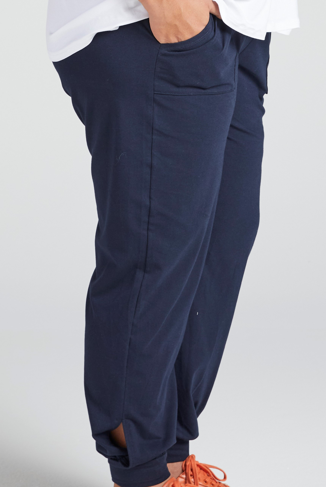 Tapered Track Pants with Adjustable Cuff shown in navy blue, featuring a relaxed fit with side pocket detail and elastic cuffs at ankles. Mid-rise waistband visible with white shirt partially tucked in, styled with orange sneaker laces.
