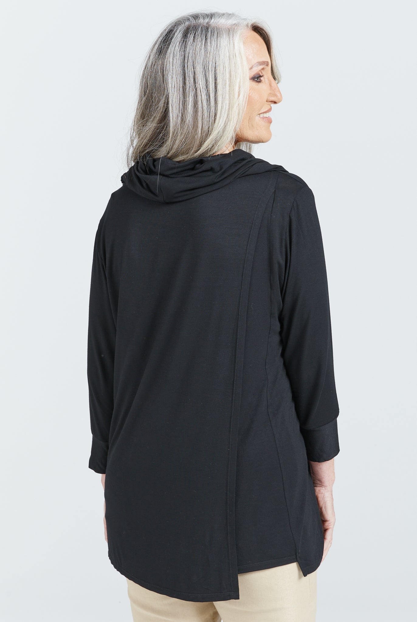 Cowl Neck Leaf Back Top shown from behind, featuring a black bamboo fabric with 3/4 length sleeves and split back design. Model has silver hair and the top drapes elegantly, showcasing the relaxed fit and luxurious flow of the garment against a white background.