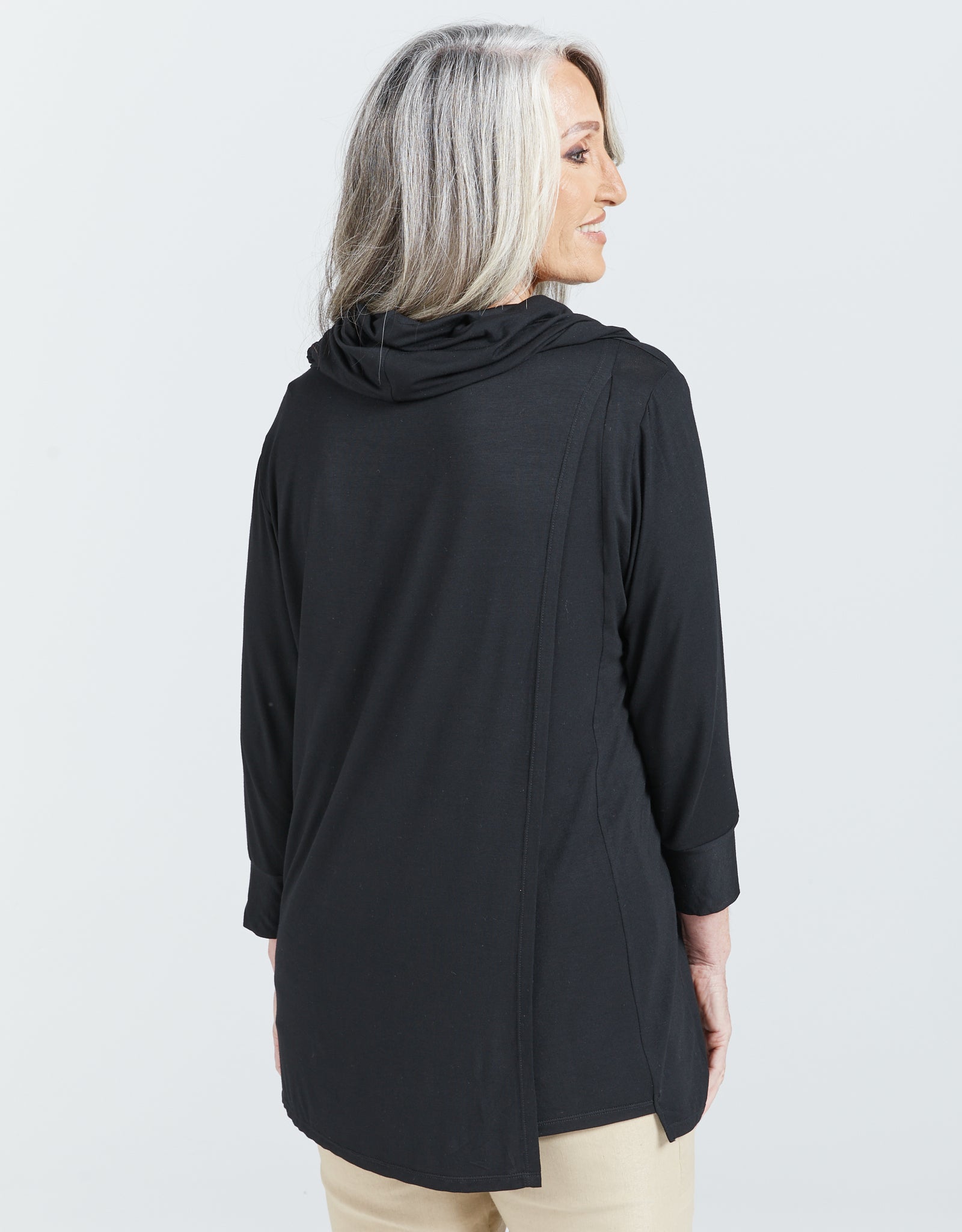 Cowl Neck Leaf Back Top shown from behind, featuring a black bamboo fabric with 3/4 length sleeves and split back design. Model has silver hair and the top drapes elegantly, showcasing the relaxed fit and luxurious flow of the garment against a white background.