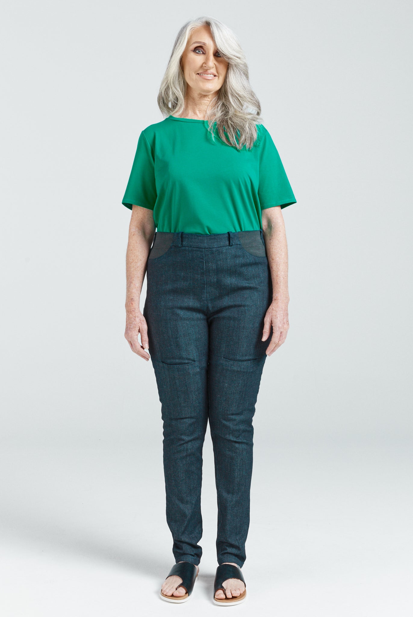 Woman wearing Women's Seated Stretch Pant - Indigo dark blue, standing and smiling, paired with green top and sandals.