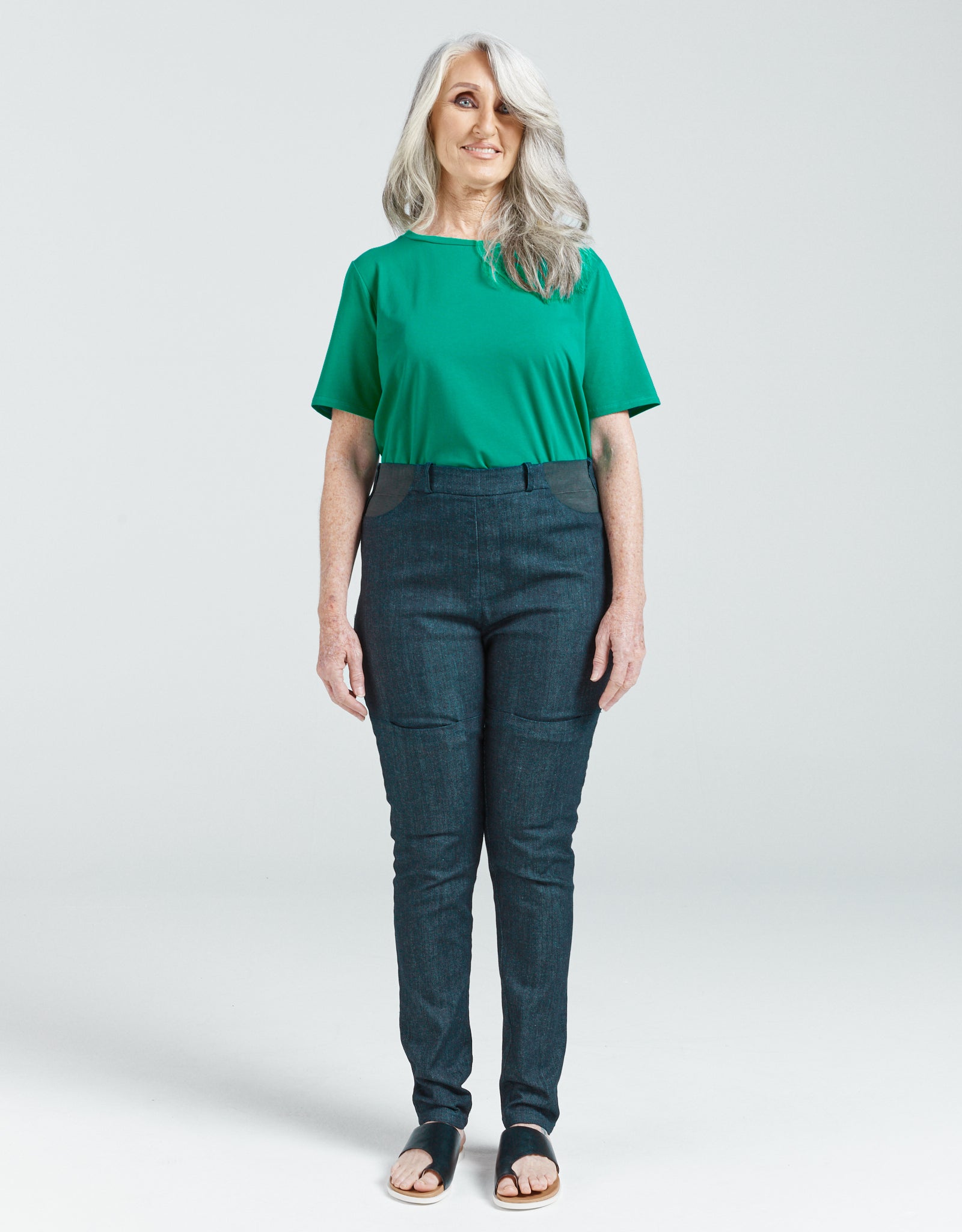 Woman wearing Women's Seated Stretch Pant - Indigo dark blue, standing and smiling, paired with green top and sandals.