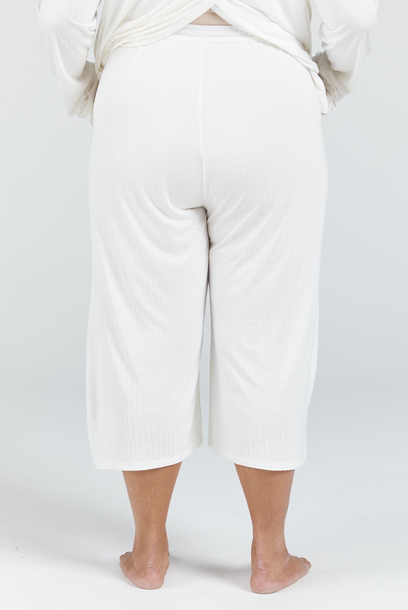 Essensual PJ Pant shown from back view in crisp white, featuring a comfortable cropped length that falls mid-calf. The relaxed-fit sleepwear pants display a smooth, flowing fabric with an elastic waistband for easy wear and comfort during rest.