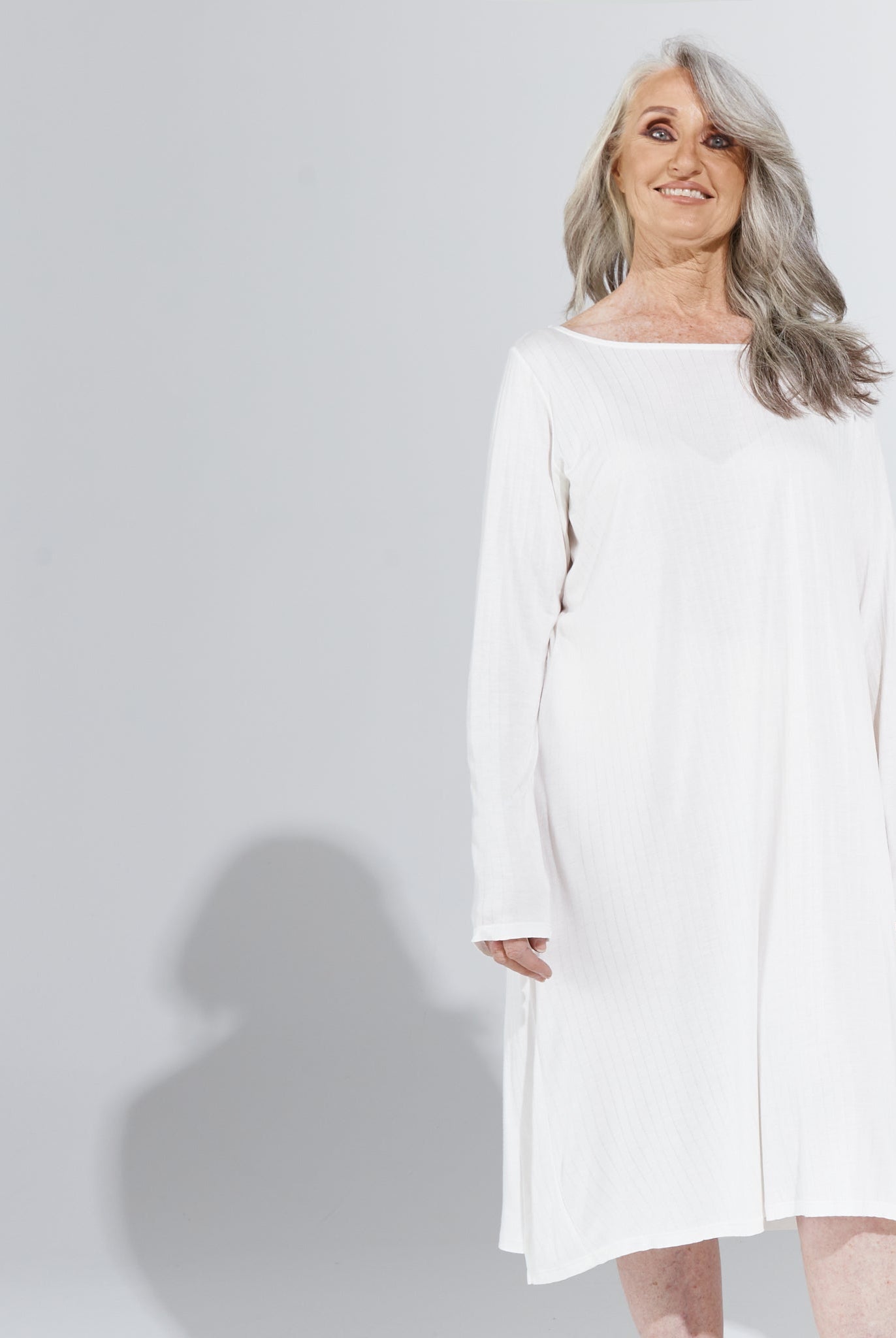 Essensual PJ Dress in crisp white, featuring a relaxed fit with long sleeves and knee-length hem. Elegant sleepwear design shown against a light gray background, highlighting the comfortable, flowing silhouette perfect for restful nights.
