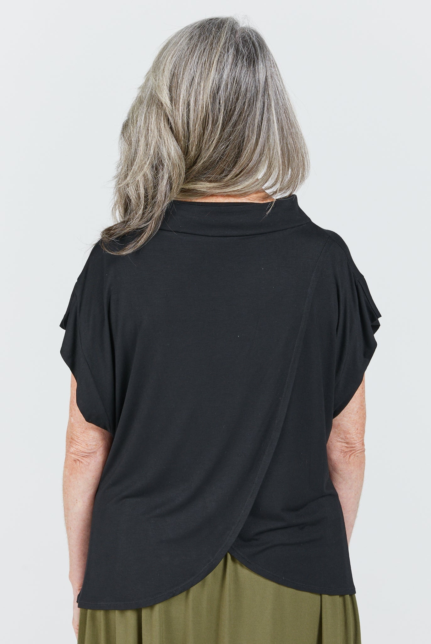 Leaf Back Blouse shown from behind, featuring elegant cross-over design in classic black with short flutter sleeves. The loose-fitting garment drapes gracefully, highlighting the Asian-inspired back detail against a light background. Gray hair showcases the neckline and shoulder construction.