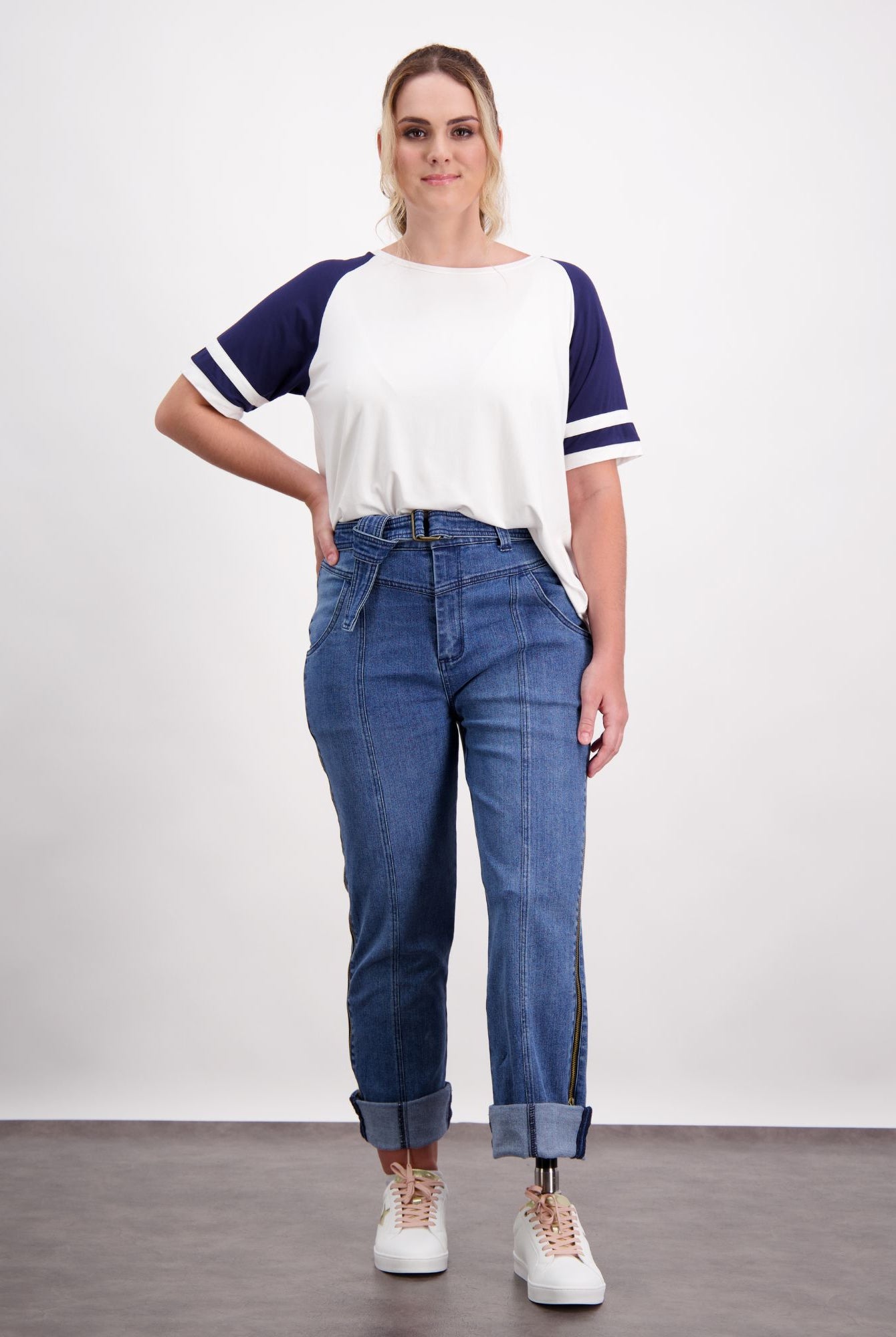 Christina Prosthetic Jeans shown in medium wash denim with unique side zippers, styled with casual white and navy baseball tee. Jeans feature specialized tear-resistant fabric and cooling technology, displayed in relaxed fit with rolled cuffs and front pockets.