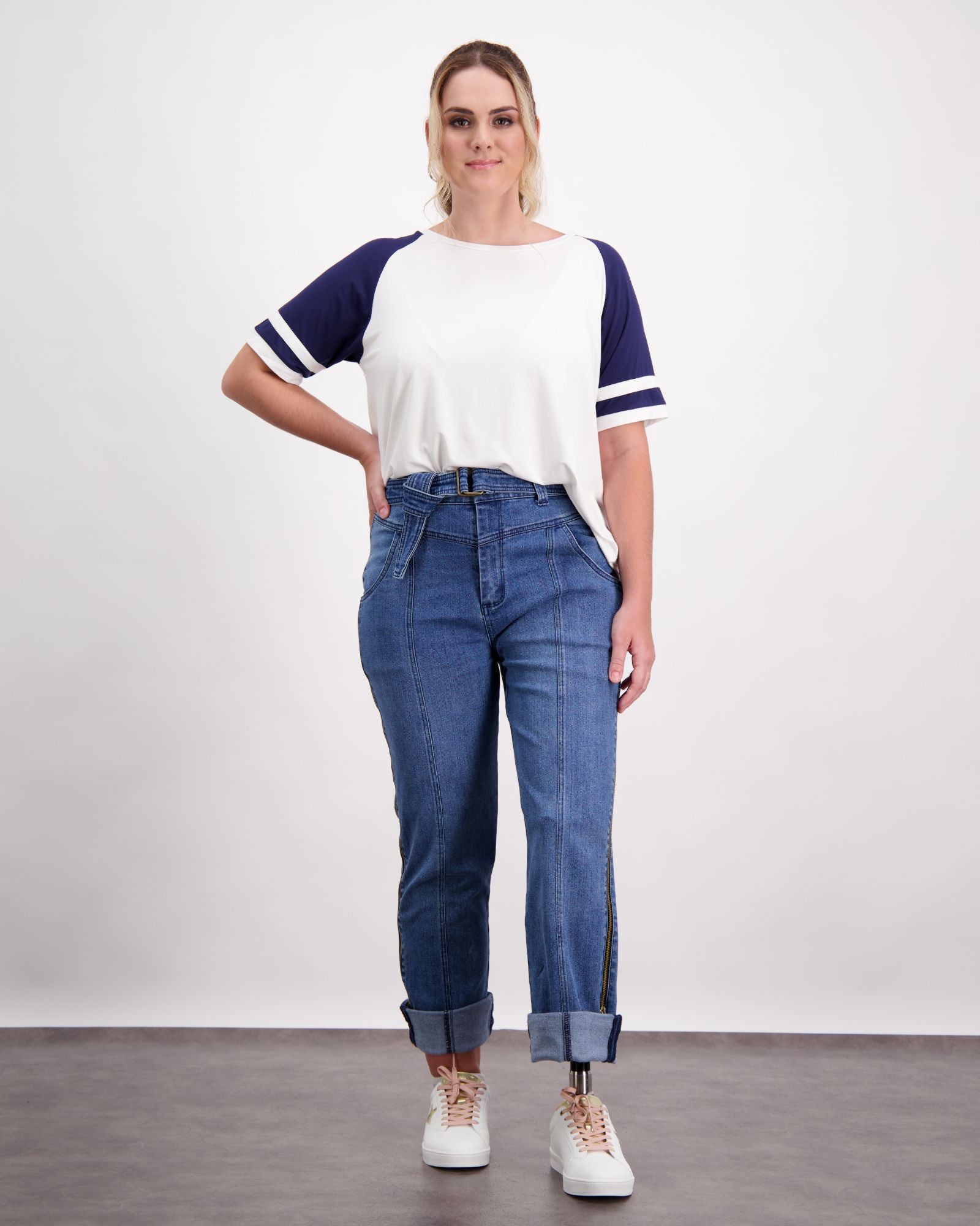 Christina Prosthetic Jeans shown in medium wash denim with unique side zippers, styled with casual white and navy baseball tee. Jeans feature specialized tear-resistant fabric and cooling technology, displayed in relaxed fit with rolled cuffs and front pockets.