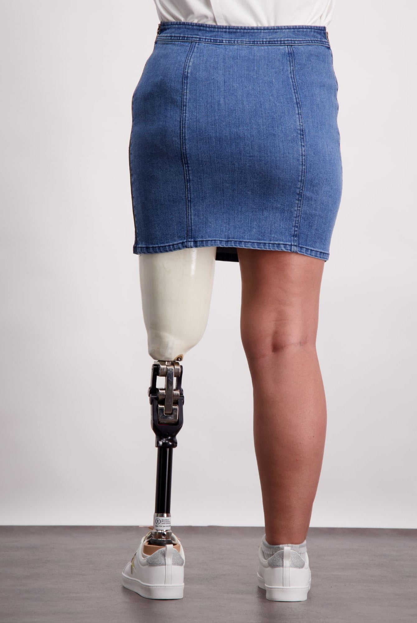 Bella Skirt shown on a model against light background, featuring quilted blue denim design with adaptive features including side zips. Skirt length hits above knee, displaying durable construction and comfortable fit. Styled with white top and casual footwear.