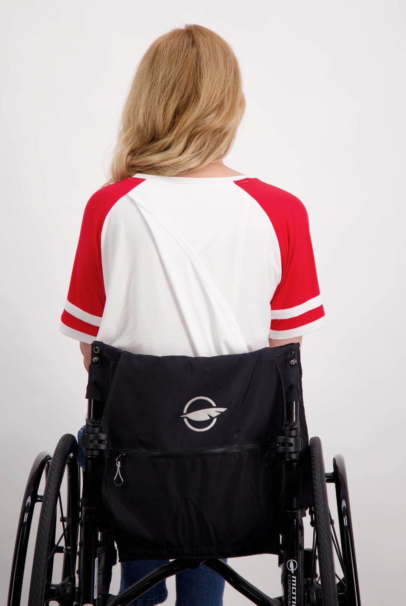 Lisa Raglan Leaf Back T-Shirt shown from behind on someone seated in a wheelchair, featuring a classic white body with red raglan sleeves and stripe details. The shirt demonstrates the casual, sporty design with a relaxed fit against a light background.