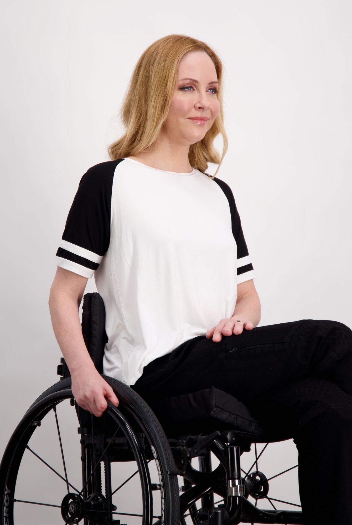 Lisa Raglan Leaf Back T-Shirt shown in classic black and white design with contrasting stripe details on sleeves. Model seated wearing casual ensemble demonstrating comfortable fit and versatile styling of this sporty raglan tee.