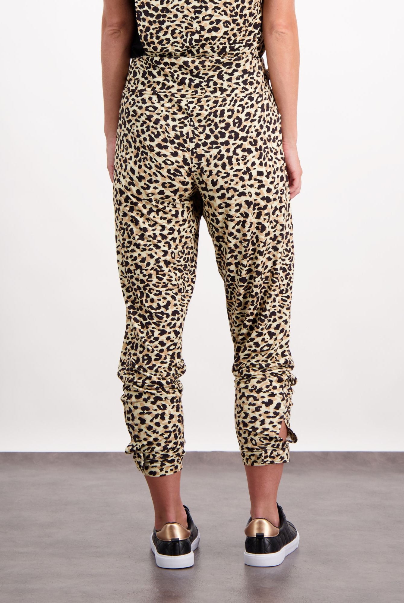 Natasha Physio Leggings in trendy leopard print pattern, shown from back view with gathered ankle detail and high waistband, paired with black and gold sneakers. Perfect for workouts or casual wear.