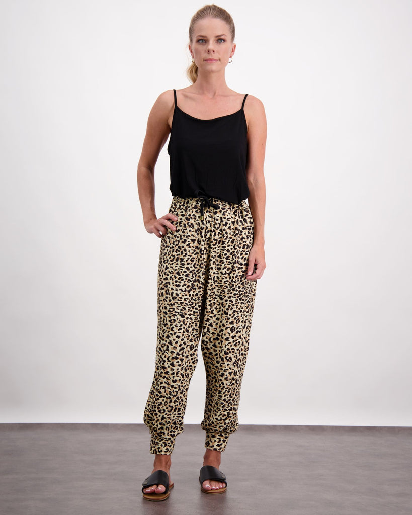 A blonde standing woman is wearing a black camiisole top, leopard print slouch pants with a black draw-string and black leather slippers.