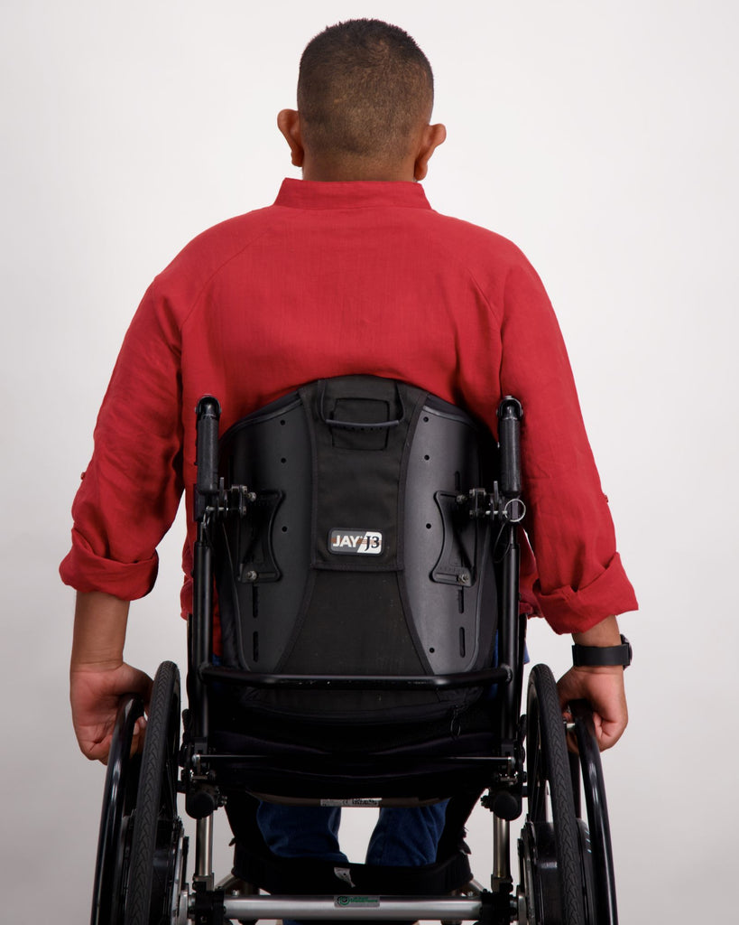 A male in a wheelchair with dark skin tone and dark hair is wearing a red linen shirt and facing backward. He is in a black coloured wheelchair. Christina Stephens Australian Adaptive Clothing.