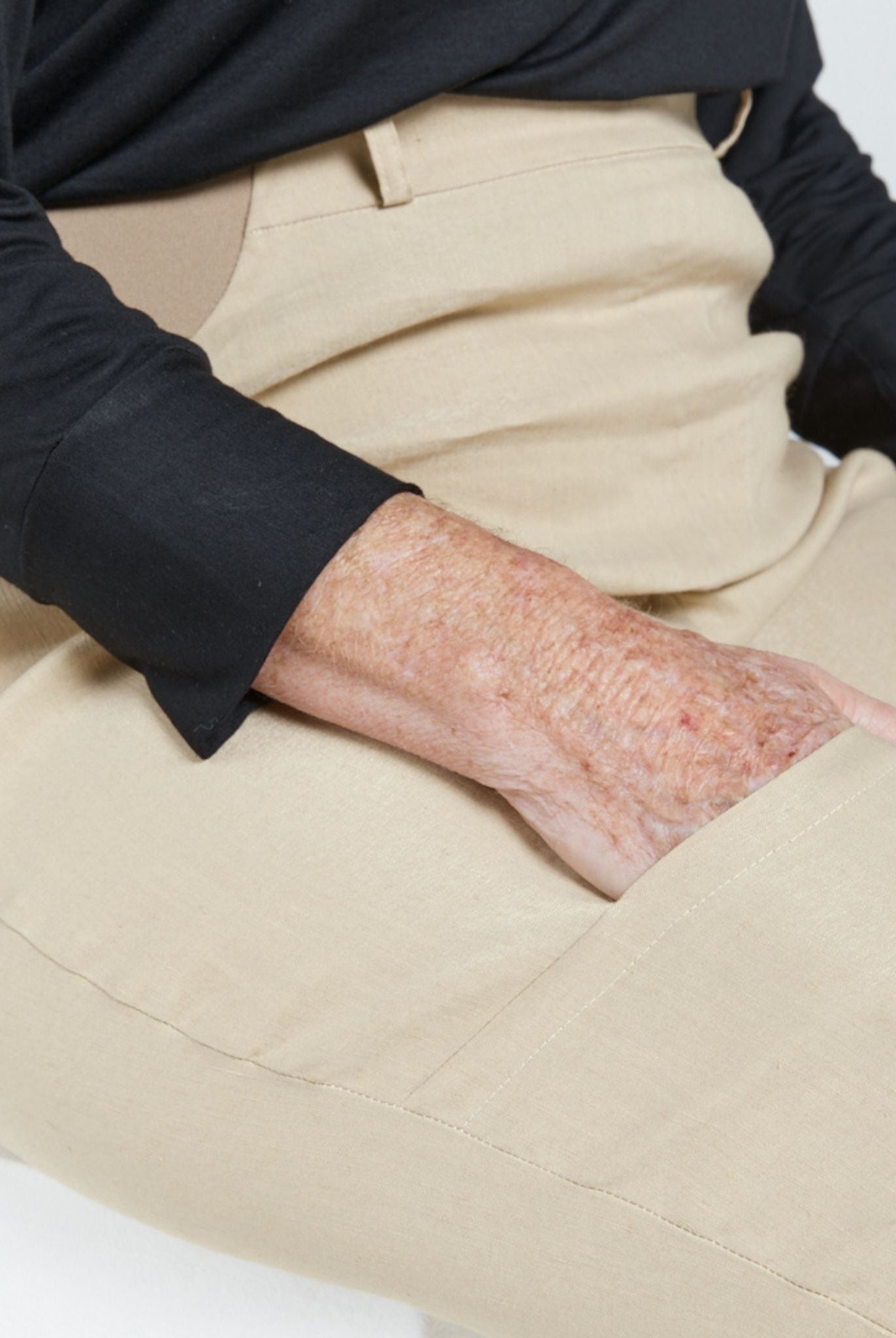 Close-up detail of the Seated Stretch Pant in beige, showing its seamless fit against a black long-sleeved top. The adaptive design features smooth fabric construction and comfortable waistband, highlighting the pant's practical yet stylish functionality.