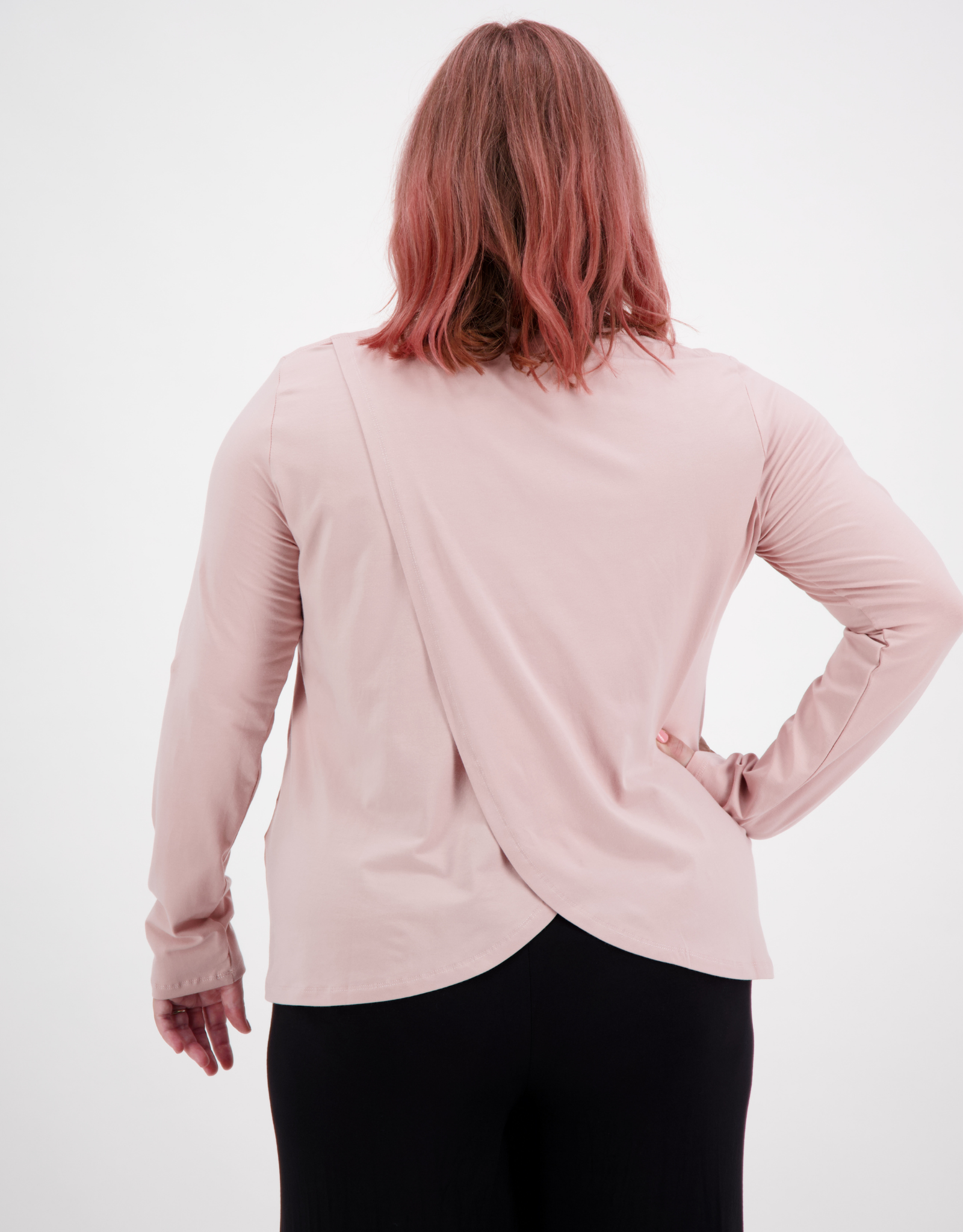 Long Sleeve Leaf Back T-Shirt in soft pink featuring unique cross-over back design, shown from rear view against white background. Stylish casual top paired with black bottoms, demonstrating the elegant drape and overlap detail of the back panel.