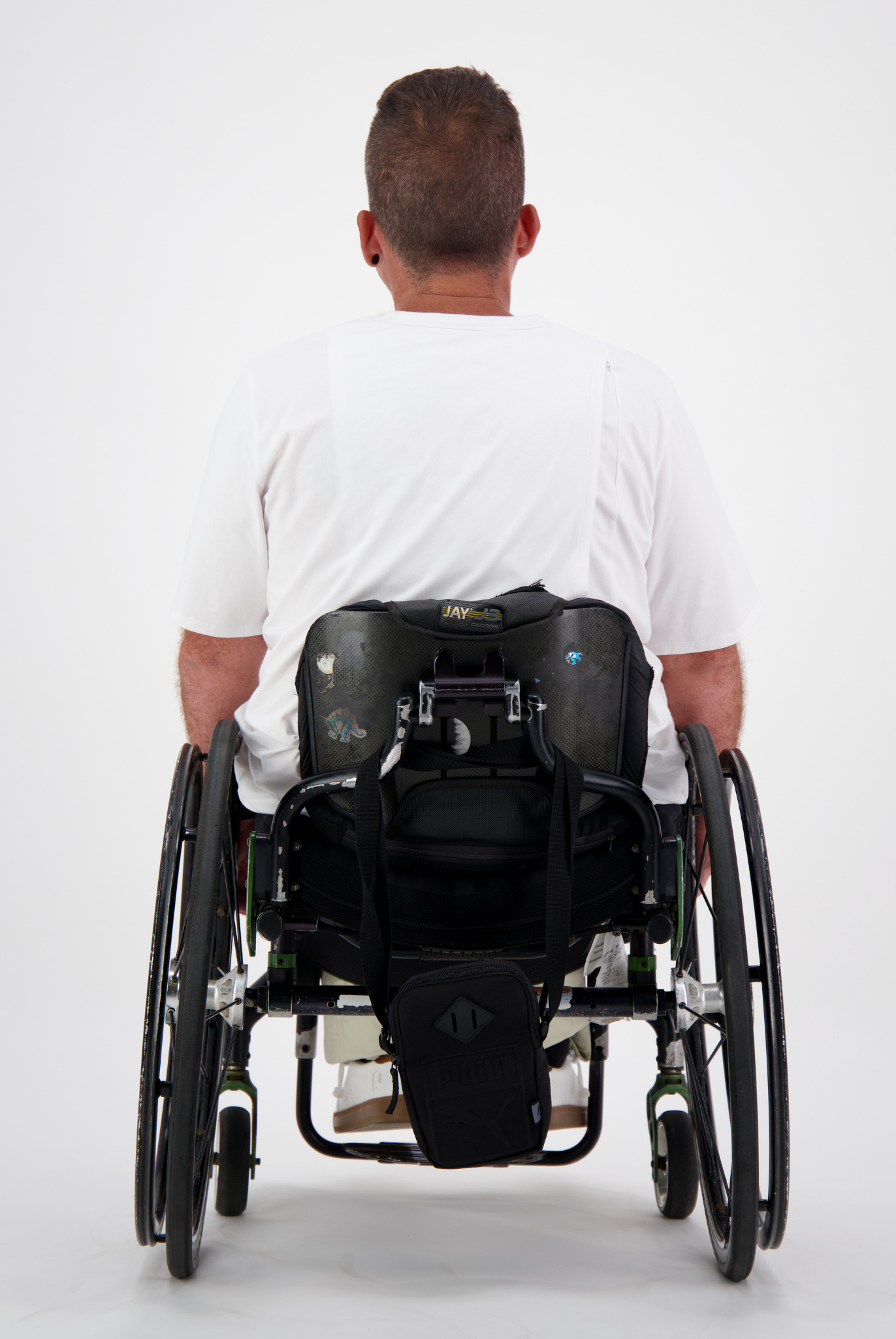 Back view of Short Sleeve Prism Back T-Shirt shown on a person using a manual wheelchair, demonstrating the shirt's clean fit and accessibility features against a white background