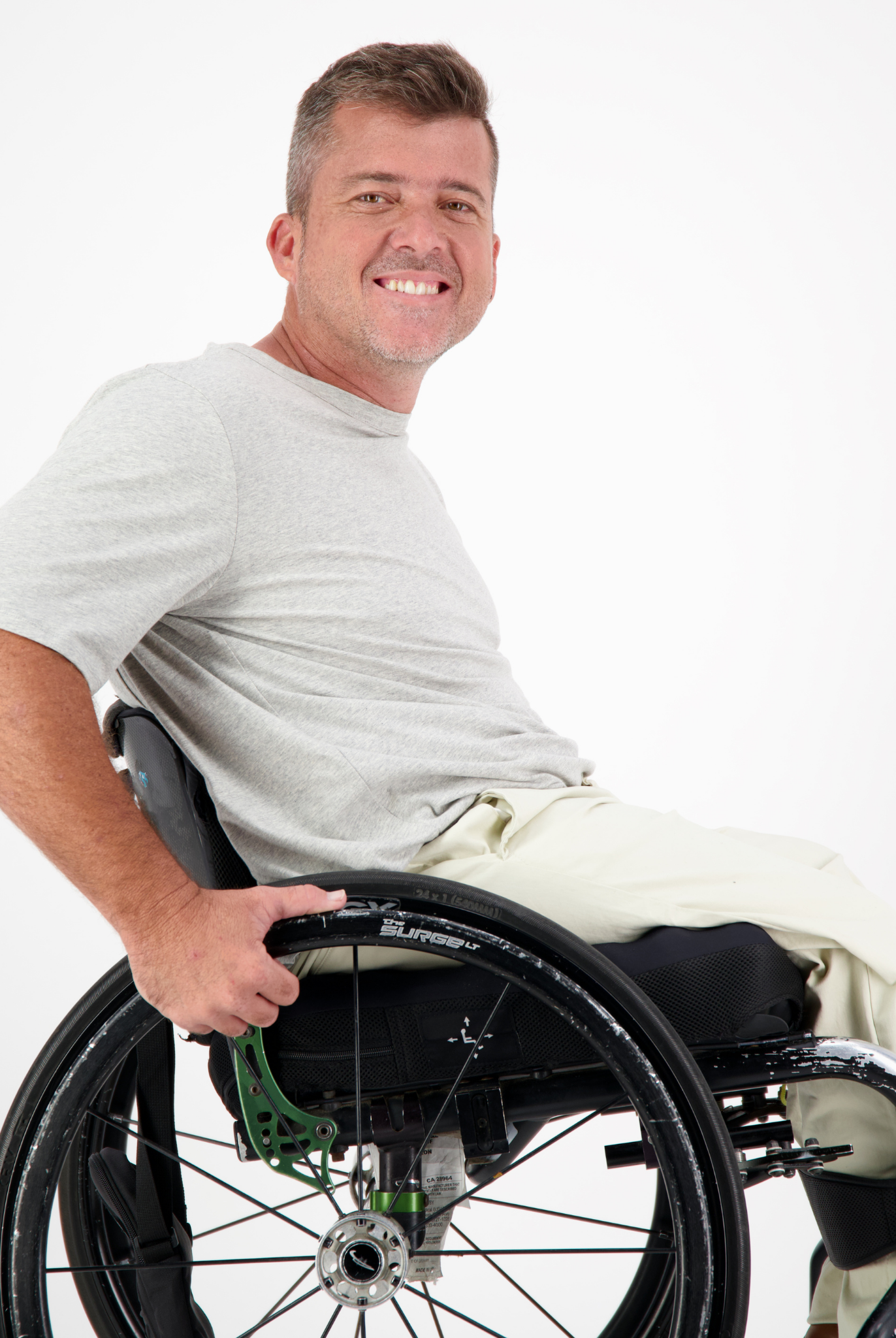 Short Sleeve Prism Back T-Shirt shown in light gray color, demonstrated on a person seated in a manual wheelchair against a white background, highlighting the shirt's casual comfort and adaptive-friendly design