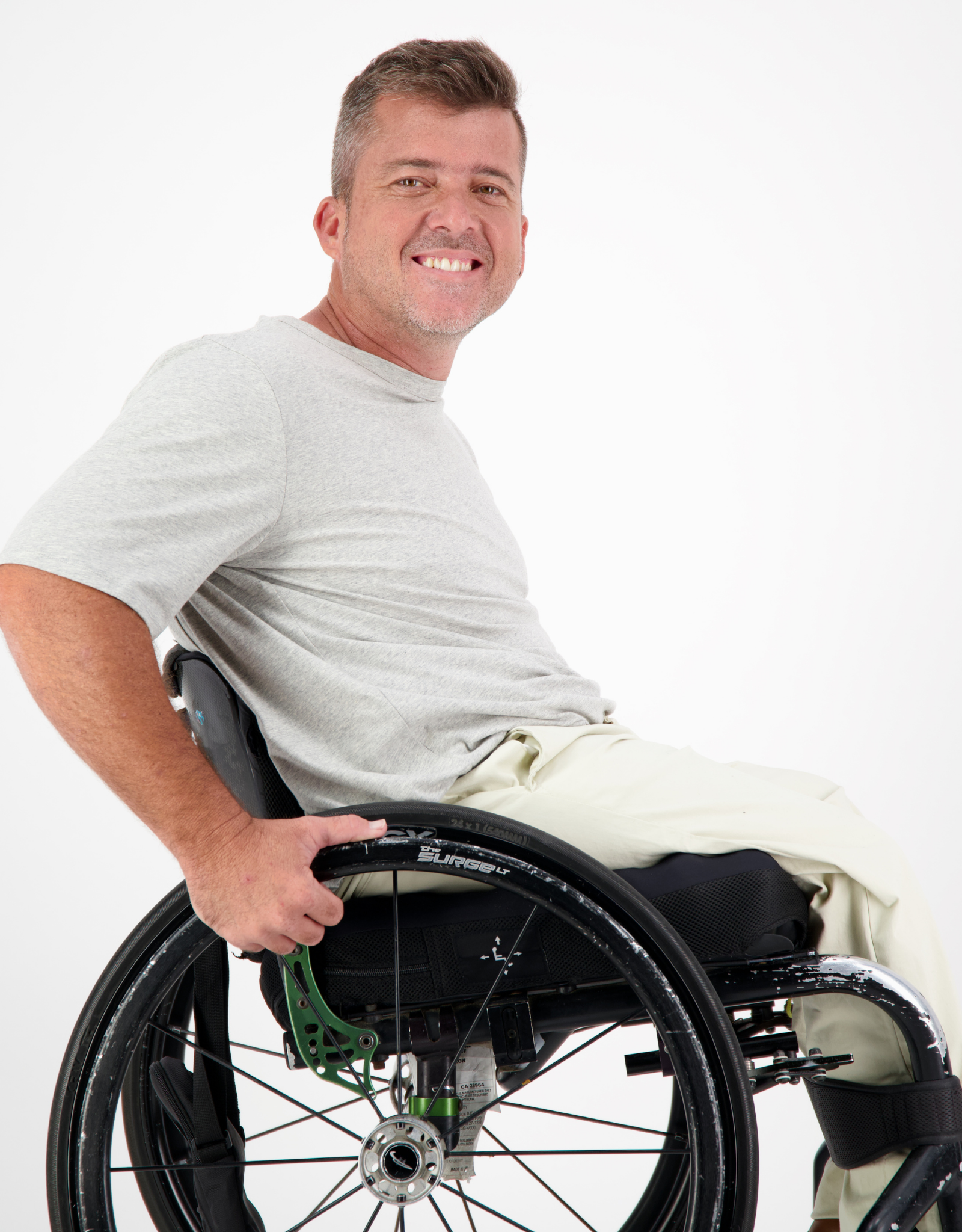 Short Sleeve Prism Back T-Shirt shown in light gray color, demonstrated on a person seated in a manual wheelchair against a white background, highlighting the shirt's casual comfort and adaptive-friendly design