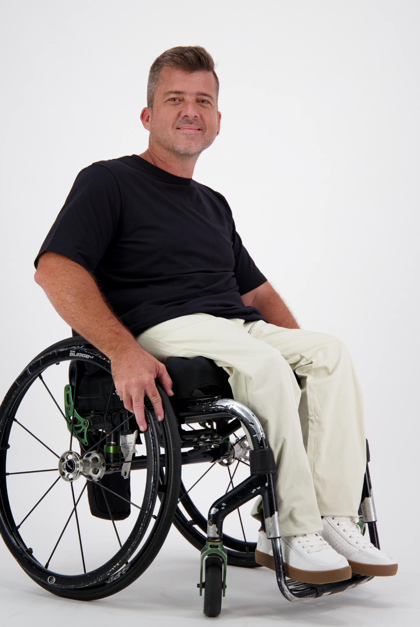 Short Sleeve Prism Back T-Shirt shown on a wheelchair user against a light background, featuring a classic black crew neck design paired with light-colored pants and white sneakers, demonstrating the shirt's casual versatility and comfortable fit.