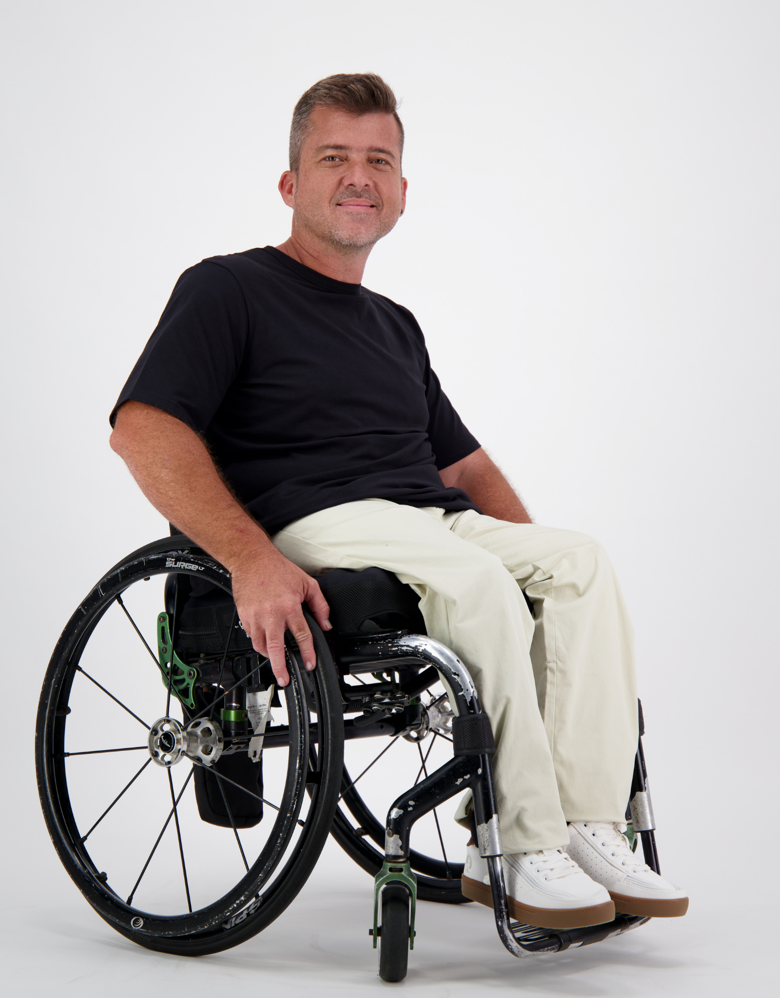 Short Sleeve Prism Back T-Shirt shown on a wheelchair user against a light background, featuring a classic black crew neck design paired with light-colored pants and white sneakers, demonstrating the shirt's casual versatility and comfortable fit.