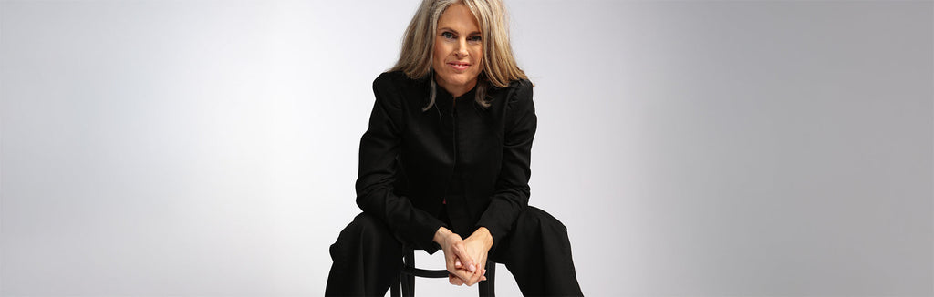 A blonde white woman with a high ponytail wears an ocean blue kaftan and black pants