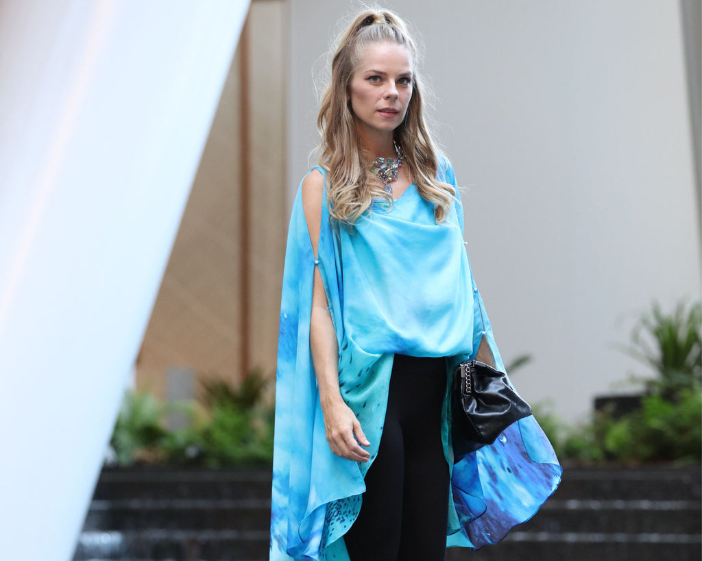 A blonde white woman with a high ponytail wears an ocean blue kaftan and black pants