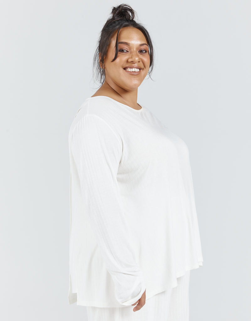 Standing female with brunette hair up in a bun is wearing an ivory bamboo leaf back top with long sleeves. She is also wearing a cropped wide leg pant made from the same fabric. Christina Stephens Adaptive Clothing Australia