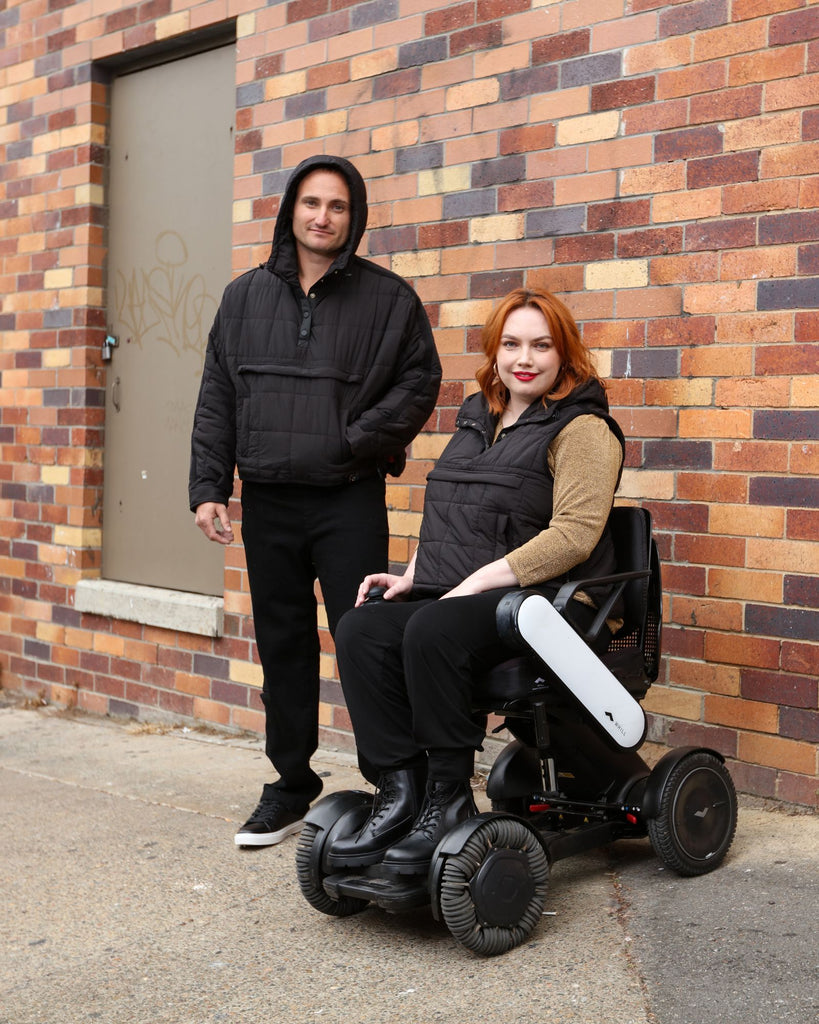 Standing male and seated female wearing midnight black puffer vest and jacket. Christina Stephens Adaptive Clothing Australia.