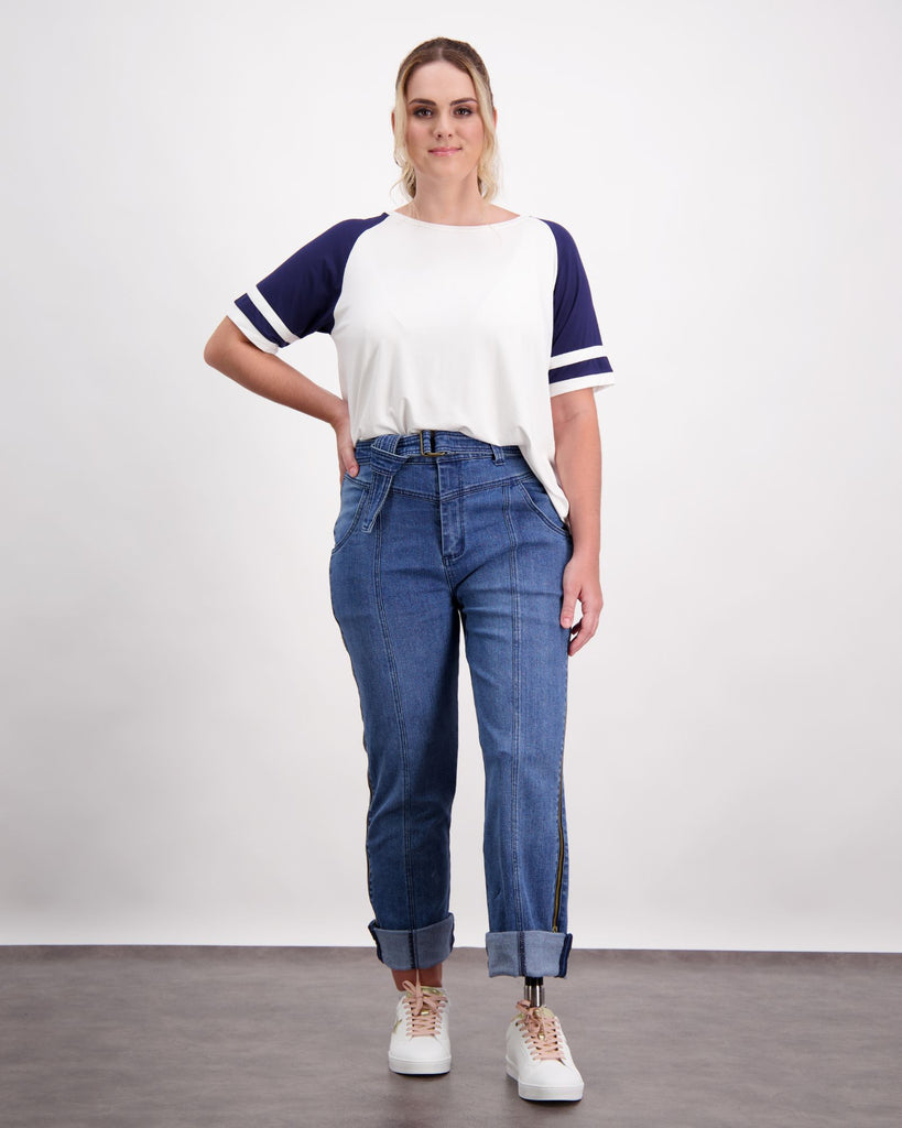 Standing female with a prosthetic limb wears a navy and white raglan leaf back t-shirt and blue jeans with white sneakers. Christina Stephens Adaptive Clothing Australia.
