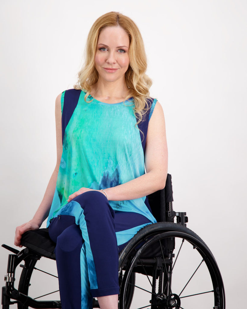 Blonde female sitting in a manual wheelchair wearing an aqua blue printed and navy sleeveless top. Christina Stephens Adaptive Clothing Australia.