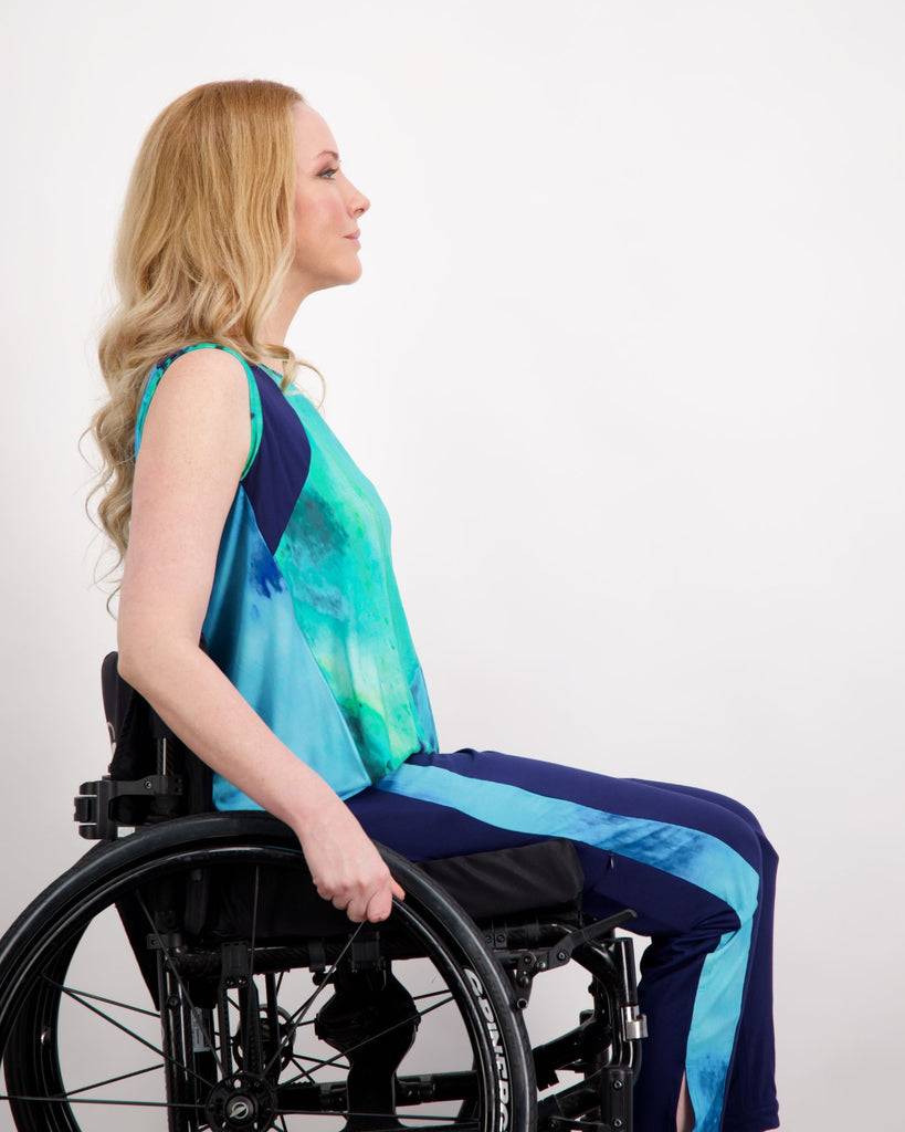 Blonde female sitting in a manual wheelchair wearing an aqua blue printed and navy sleeveless top. Side facing.Christina Stephens Adaptive Clothing Australia.