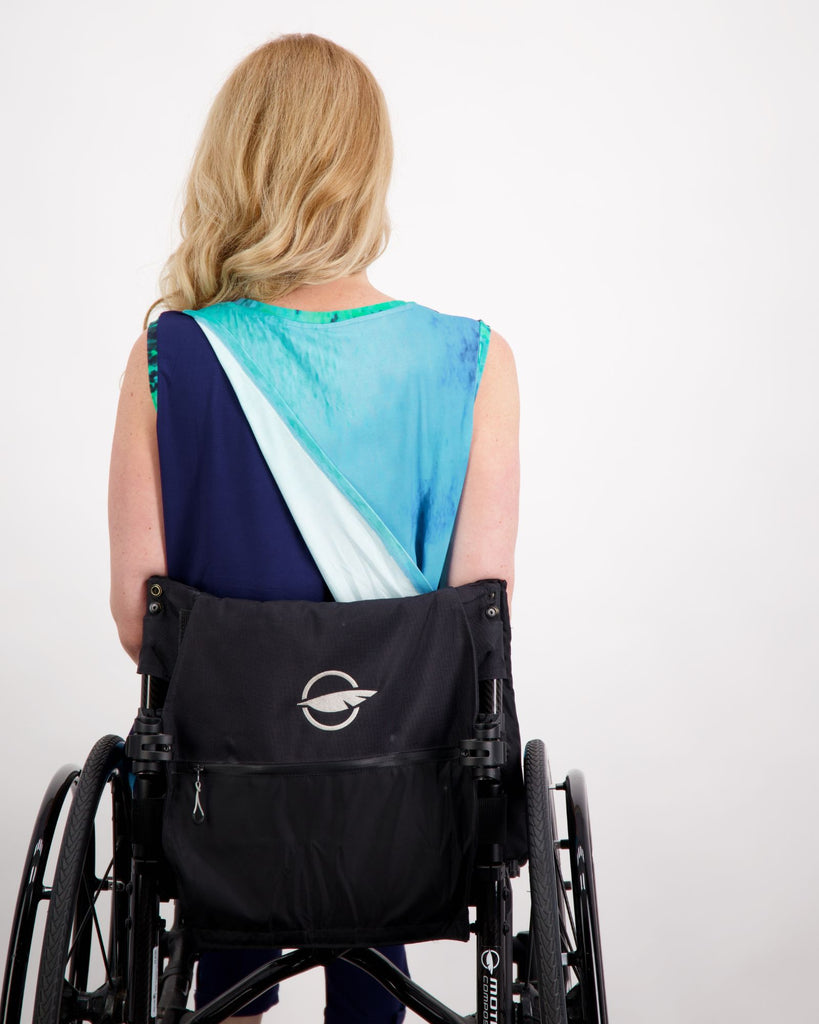 Blonde female sitting in a manual wheelchair wearing an aqua blue printed and navy sleeveless top. She is facing the back showing off the leaf back opening on the top.Christina Stephens Adaptive Clothing Australia.