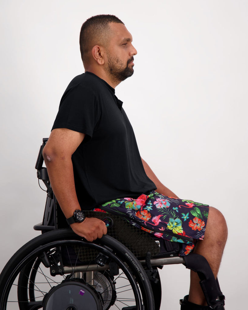 Male in a wheelchair wearing a black t-shirt and colourful boardshorts. Christina Stephens Adaptive Clothing Australia. 